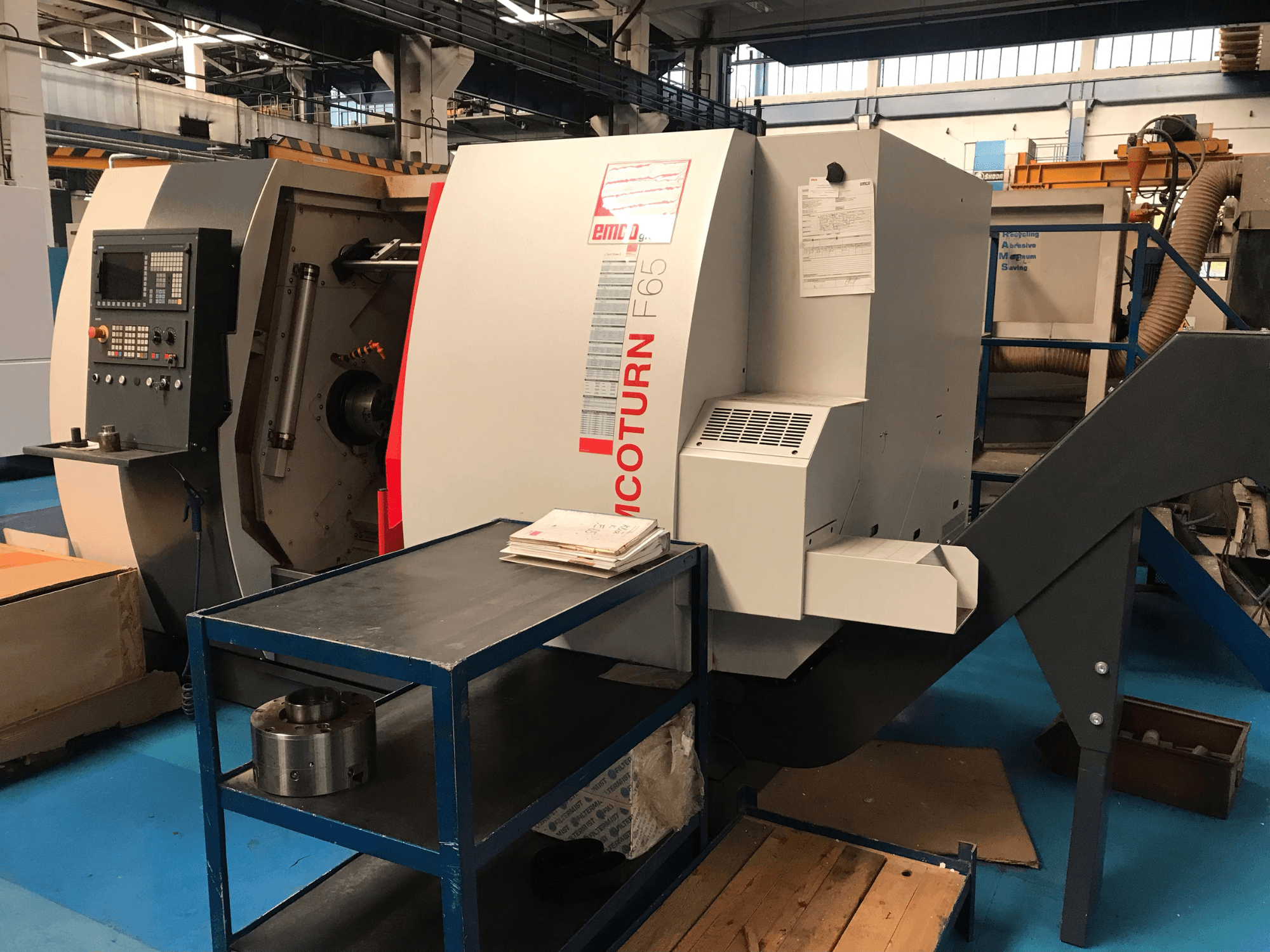 De EMCO Emcoturn 65 horizontale draaibank gezien vanaf de zijkant, met de bedieningselementen en de werkruimte in beeld, met metalen onderdelen ernaast.