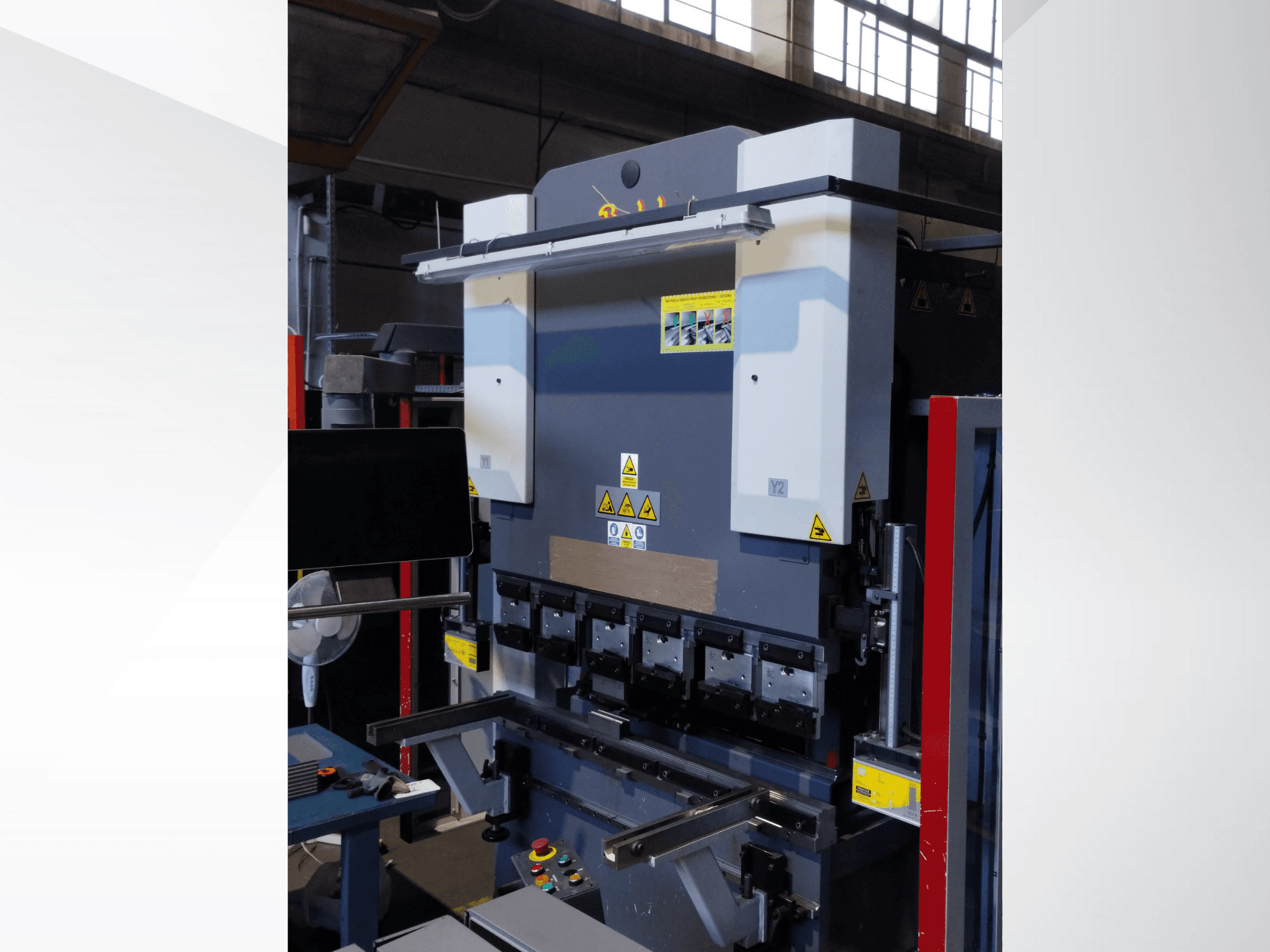 Kantpersmachine, vooraanzicht. Voorzien van zichtbare bedieningselementen, veiligheidsstickers en meerdere matrijshouders voor nauwkeurig buigen.