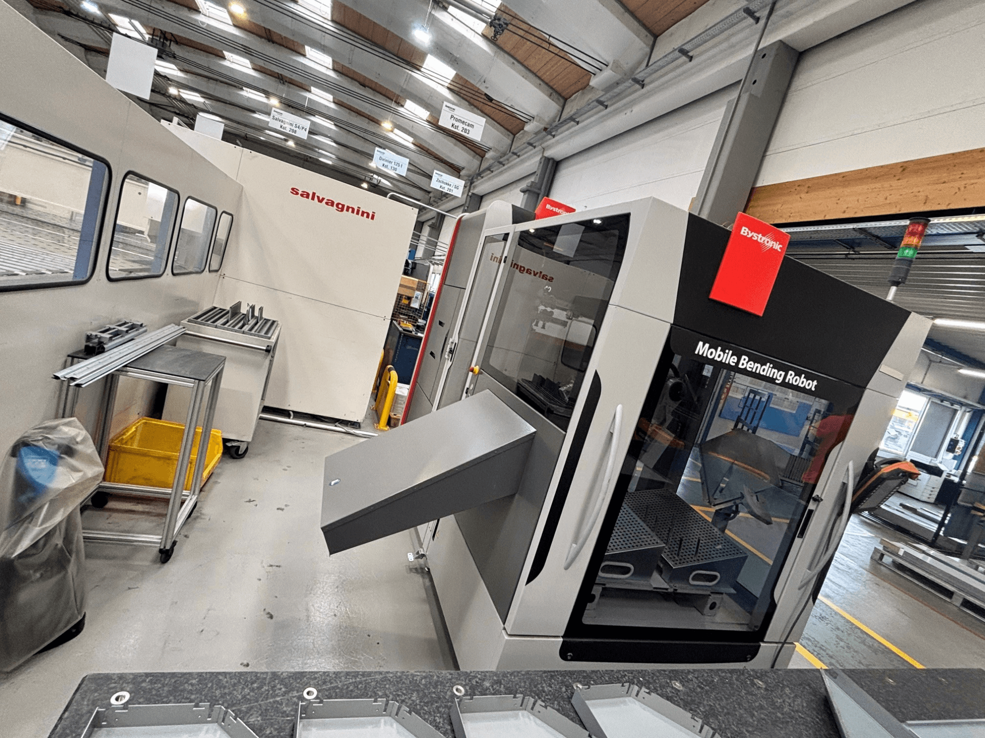 Bystronic Xpert 40/1030 kantpers, vooraanzicht met mobiele buigrobot en werkruimte met metalen onderdelen op een tafel.