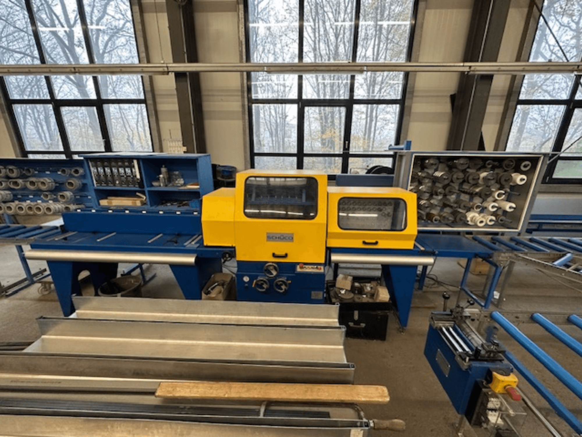 Vooraanzicht van de SCHÜCO ISOMAT 4 werktuigmachine, met een geel bedieningspaneel, meerdere rollen en een opbergvak.