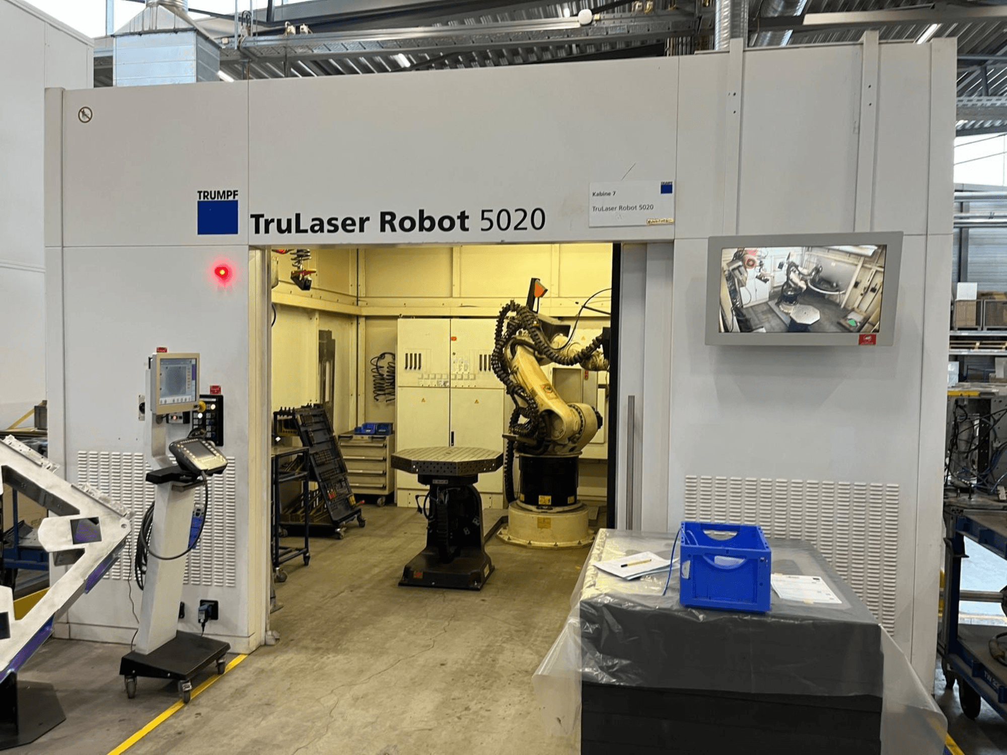 De TRUMPF TruLaser Robot 5020 in een industriële omgeving, met bedieningselementen, een robotarm en een monitor waarop de bewerkingen worden weergegeven.