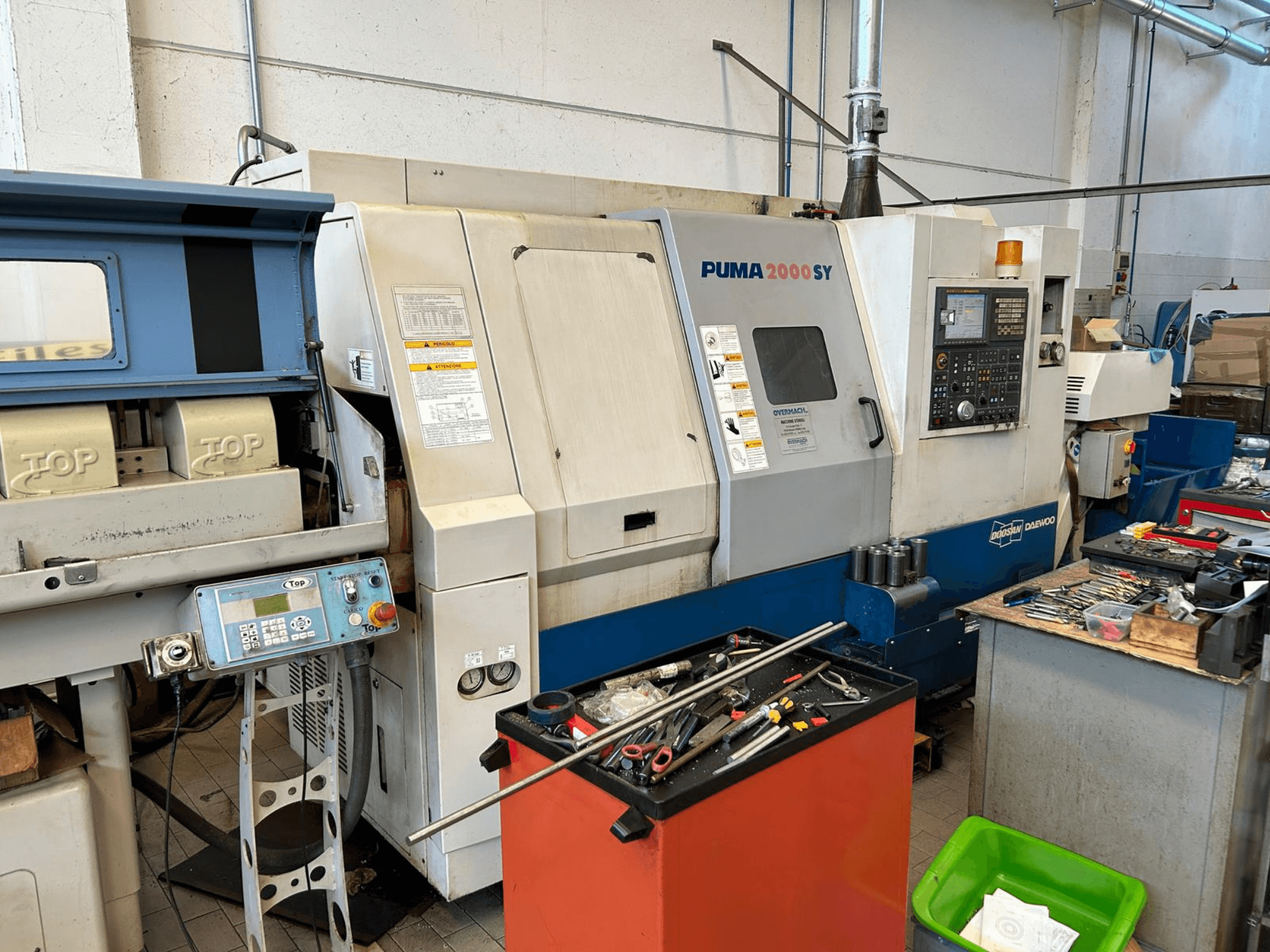 DOOSAN PUMA 2000SY horizontale draaibank in een werkplaats, zijaanzicht met het bedieningspaneel en gereedschap ernaast.
