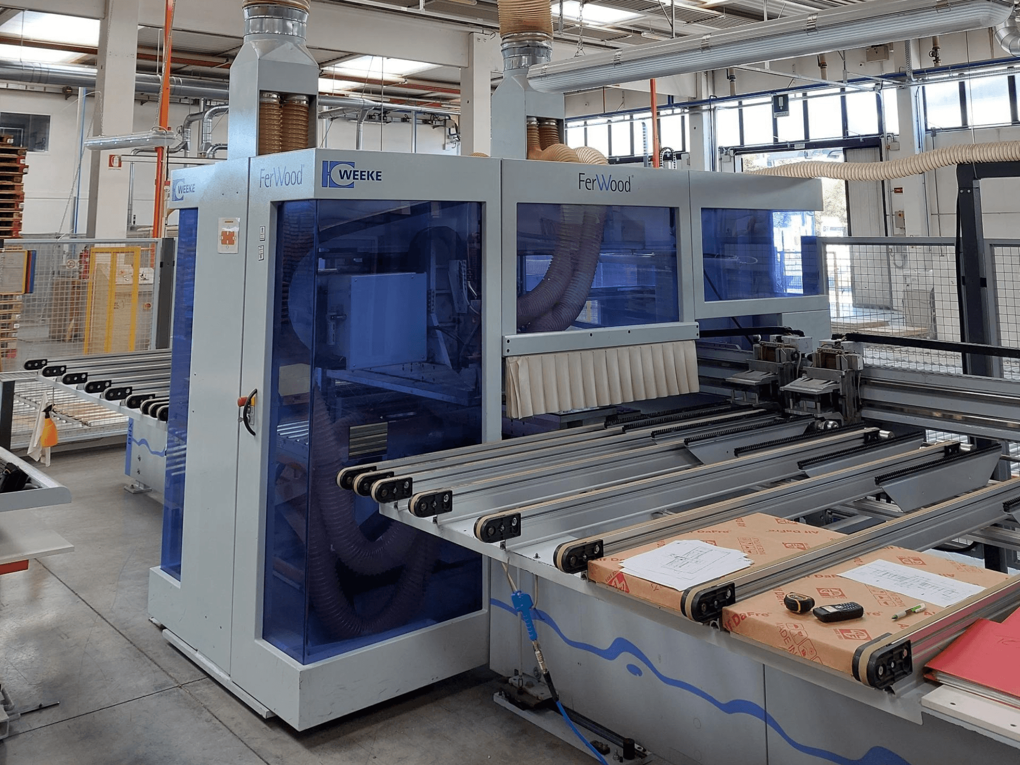 Weeke FerWood CNC machine in een werkplaats, vooraanzicht met blauwgetinte panelen, bedieningsknoppen en werktafel met materialen.