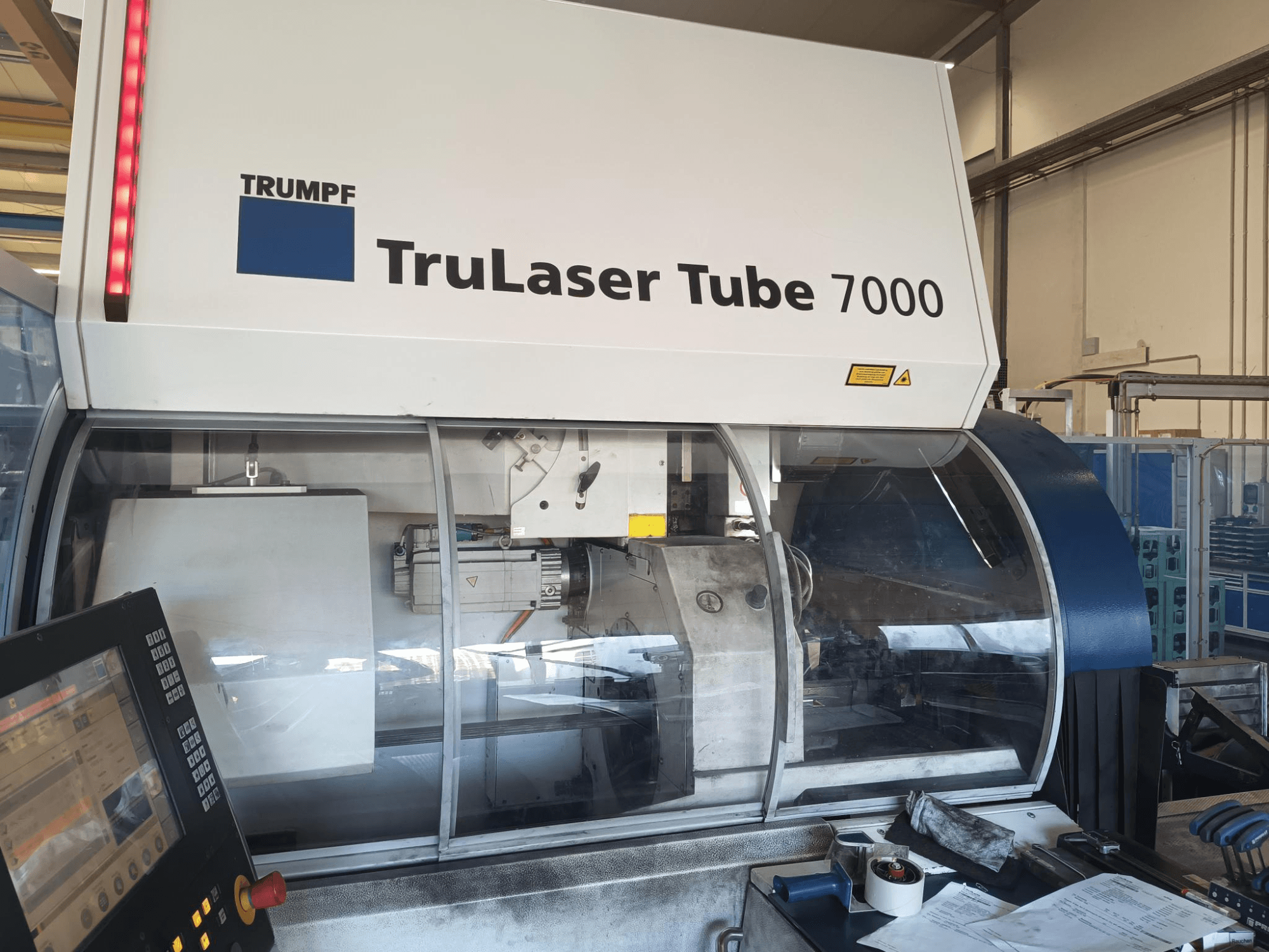 TRUMPF TruLaser Tube 7000, vooraanzicht van machine met bedieningspaneel, presentatie van lasersnijfuncties en werkruimte.