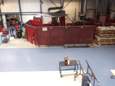 Industriële werkruimte met rode lasgordijnen, machines en pallets; bovenaanzicht van indeling en apparatuur.