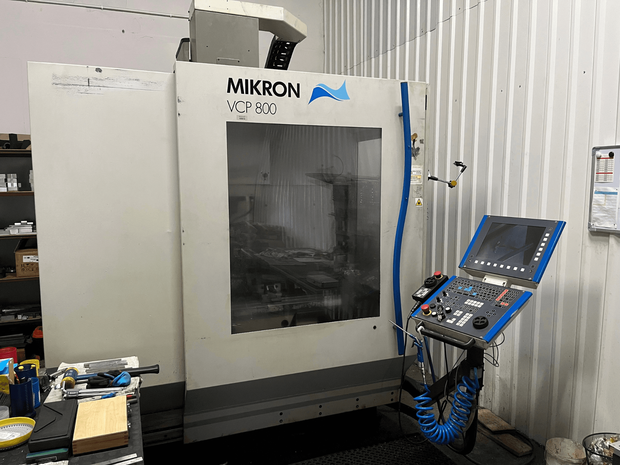 MIKRON VCP 800 verticaal bewerkingscentrum, vooraanzicht, met bedieningspaneel en gereedschappen op een werkbank op de voorgrond.
