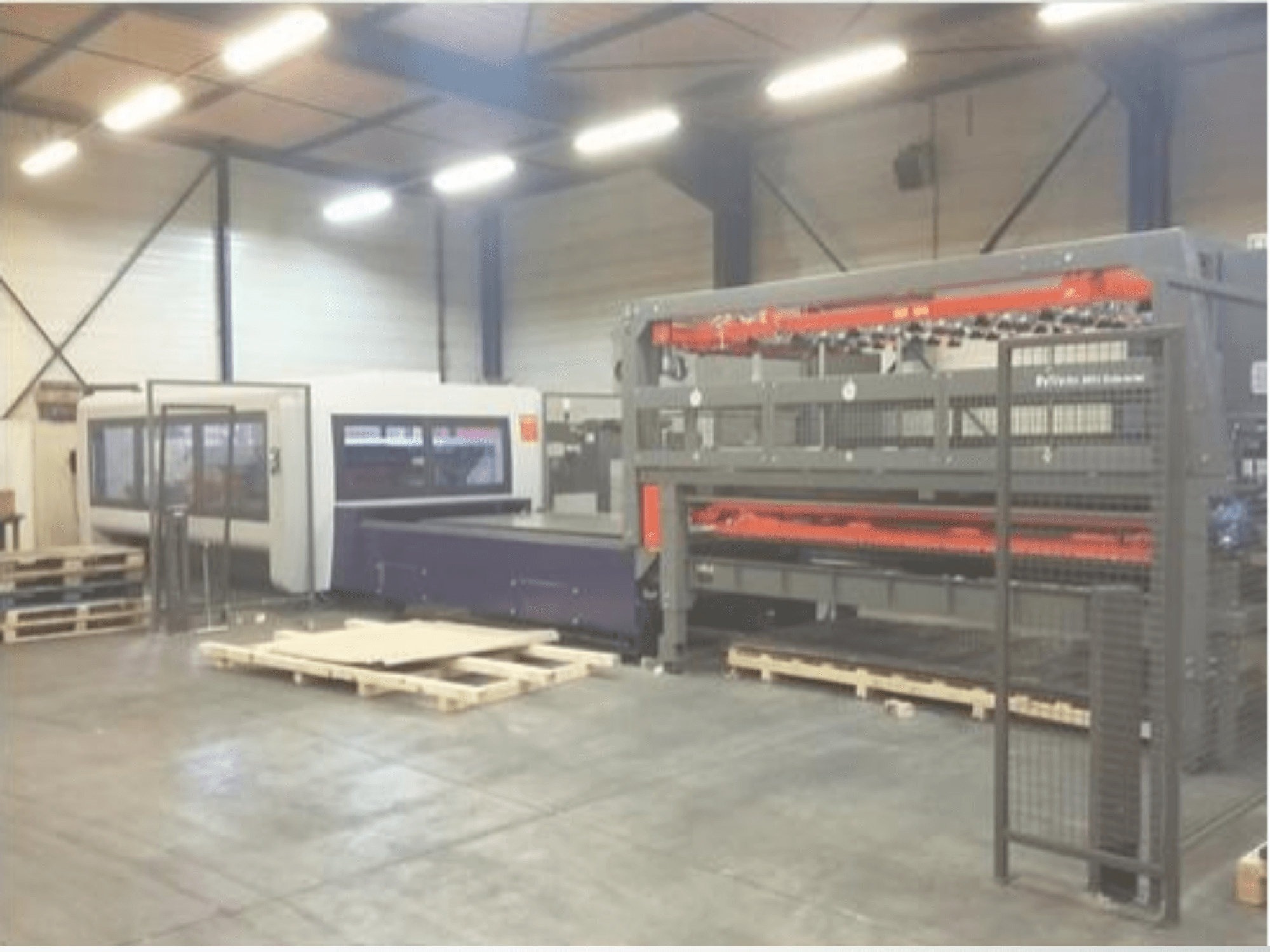 Opstelling van industriële machines in een magazijn; bevat een grijze lasersnijder en een paarse CNC-router, vooraanzicht met pallets.