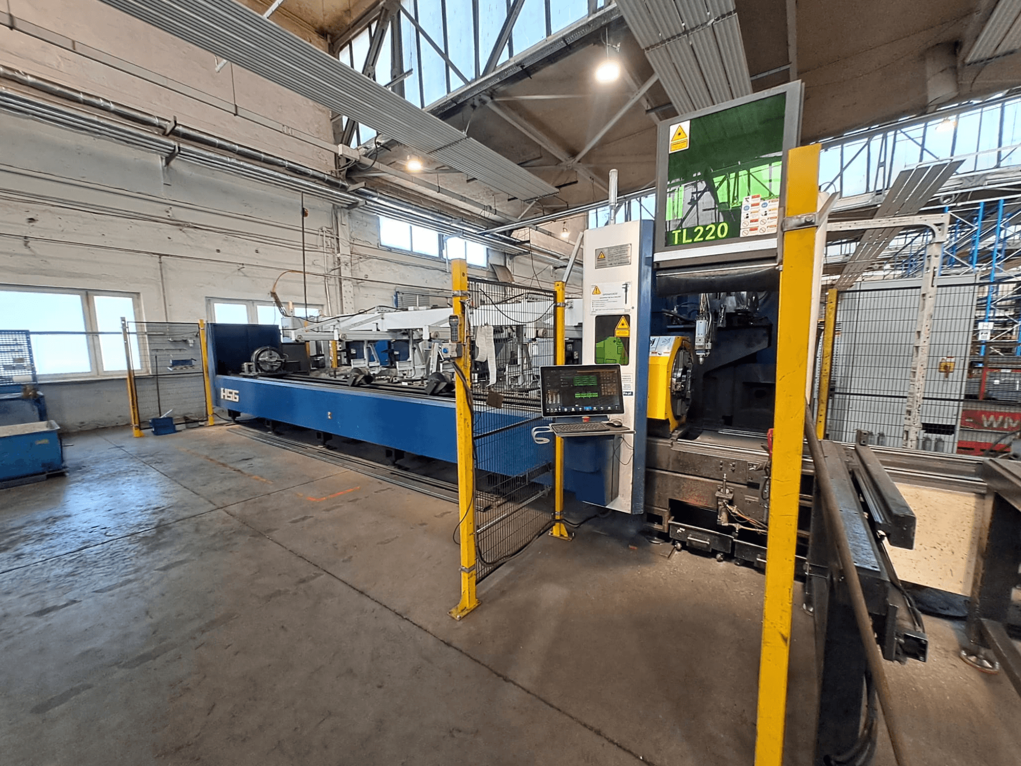 Vooraanzicht van de HSG HS-TL220 buizensnijmachine met bedieningspaneel en veiligheidshekken in een fabrieksomgeving.
