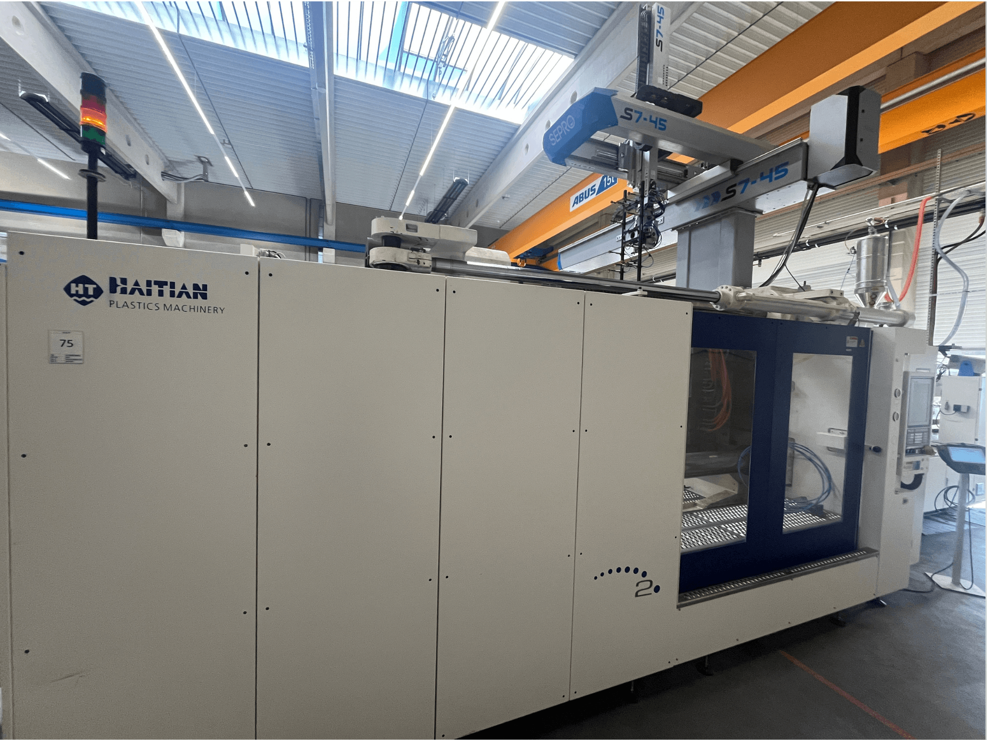 Haïtiaanse S7-45 spuitgietmachine in zijaanzicht met bedieningspaneel en veiligheidslichtindicator. Wit en blauw ontwerp.