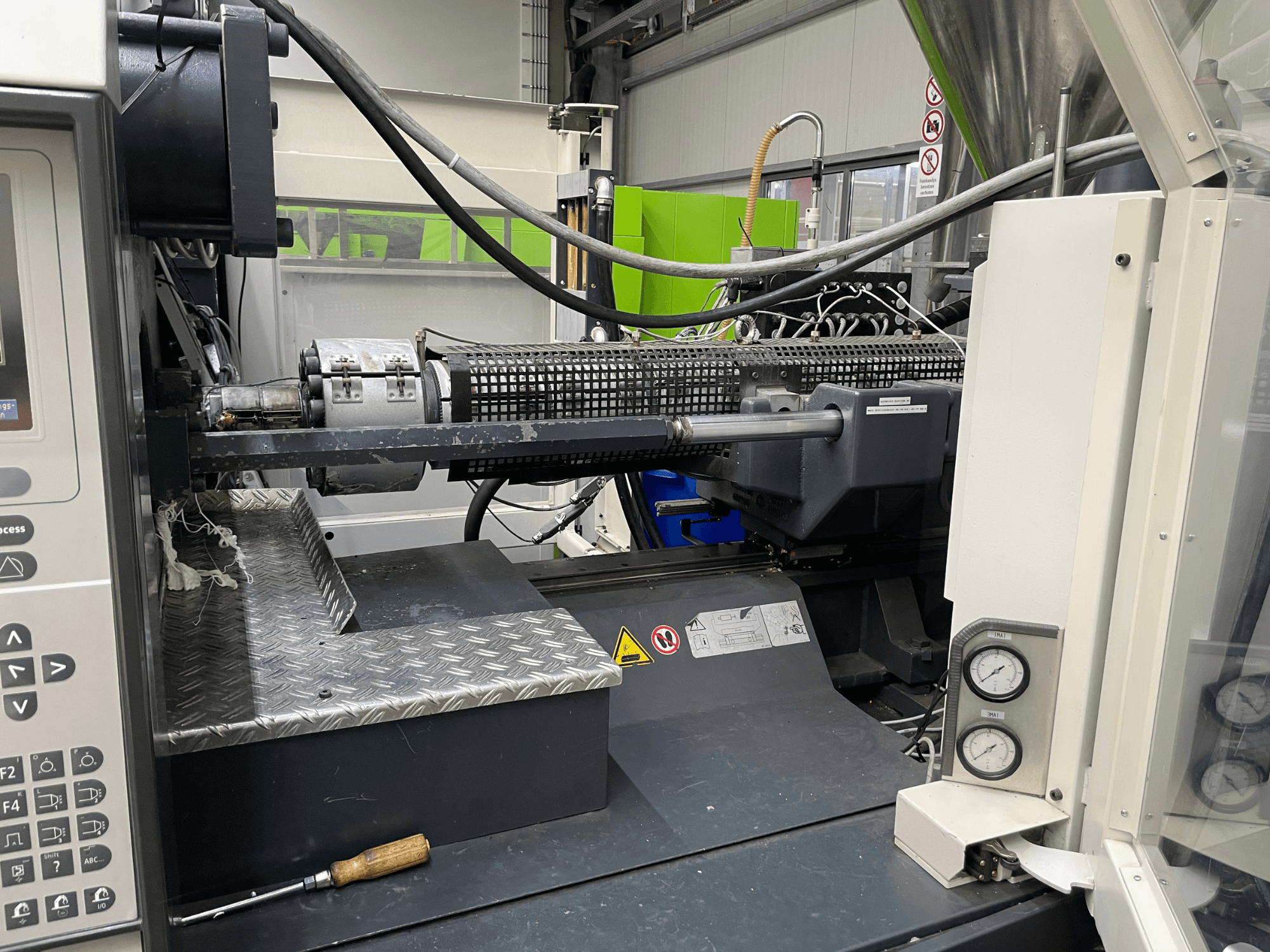 Zijaanzicht van spuitgietmachine met zichtbaar bedieningspaneel, extruder en drukmeters, ideaal voor productietaken.