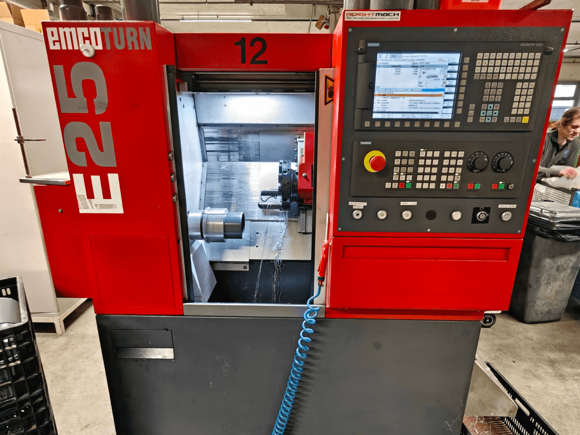 Vooraanzicht van de EMCO TURN E25 machine, met het bedieningspaneel, de gereedschapshouder en de binnenruimte waarin het snijgereedschap zichtbaar is.