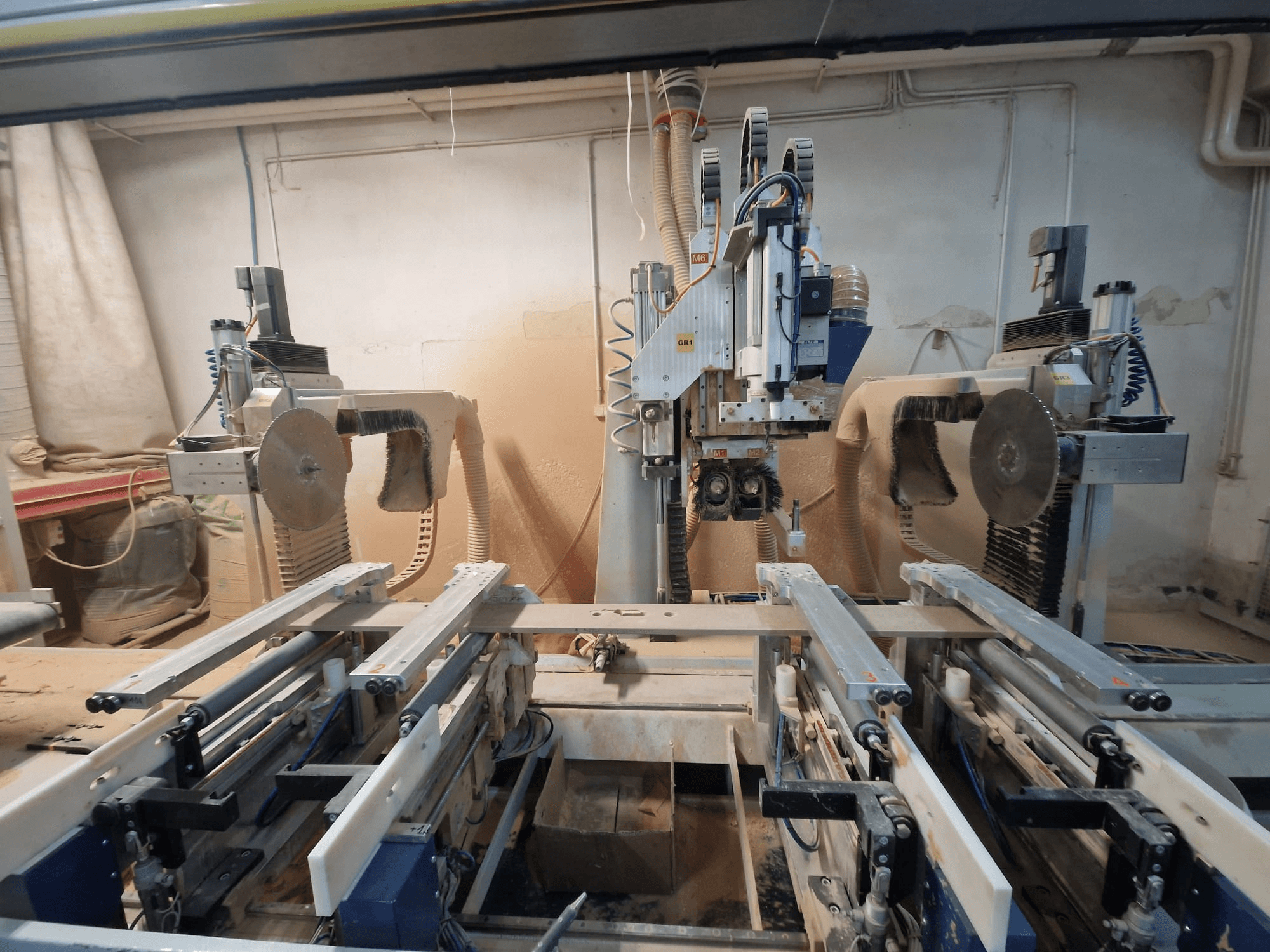 CNC machine met dubbele zaagbladen en rails, gezien vanaf de voorkant. Stofafzuigsystemen zichtbaar, geschikt voor houtbewerking.