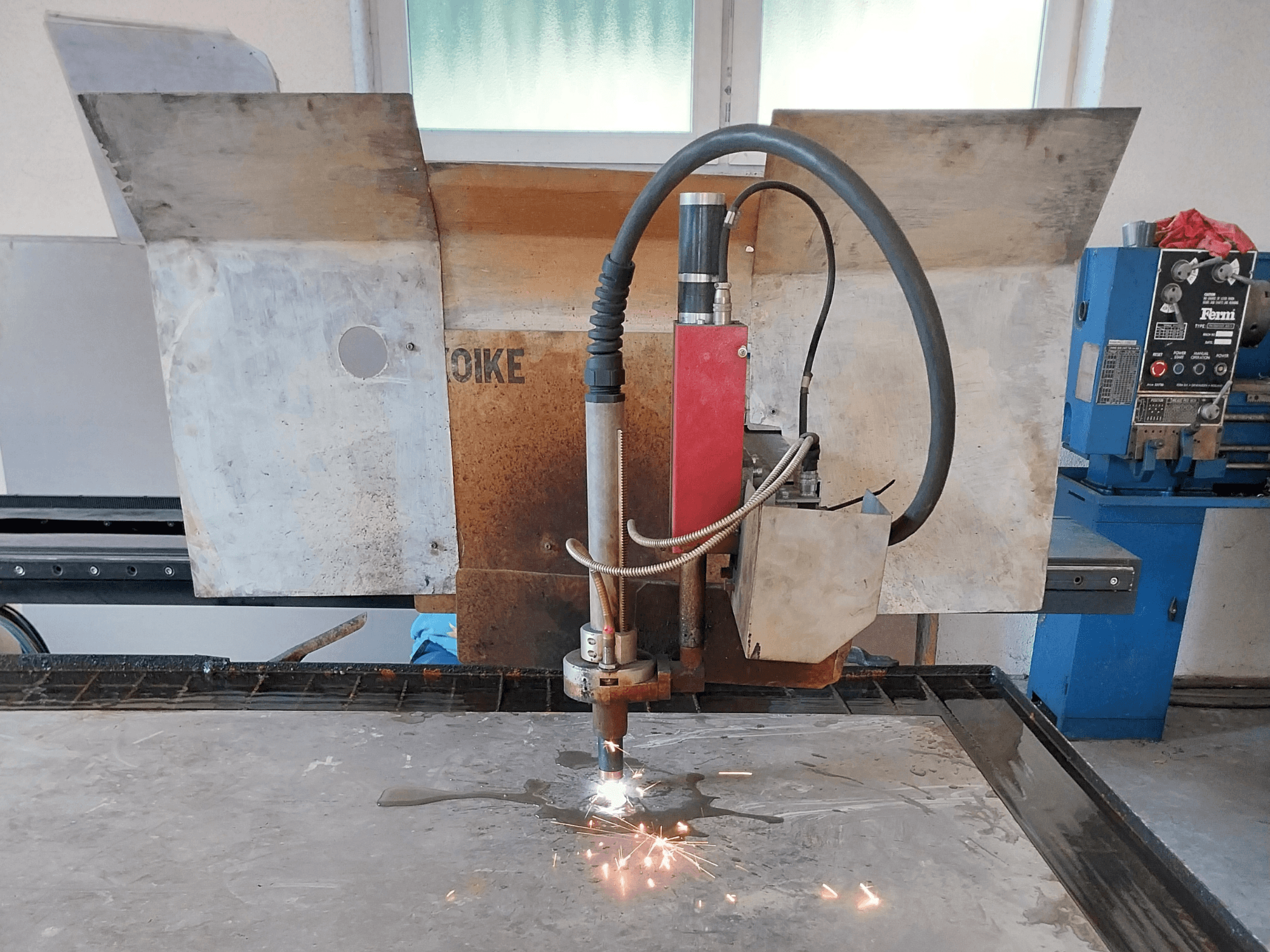 Een vooraanzicht van een Oike plasmasnijder met rondvliegende vonken, geplaatst boven een metalen oppervlak op een werktafel.