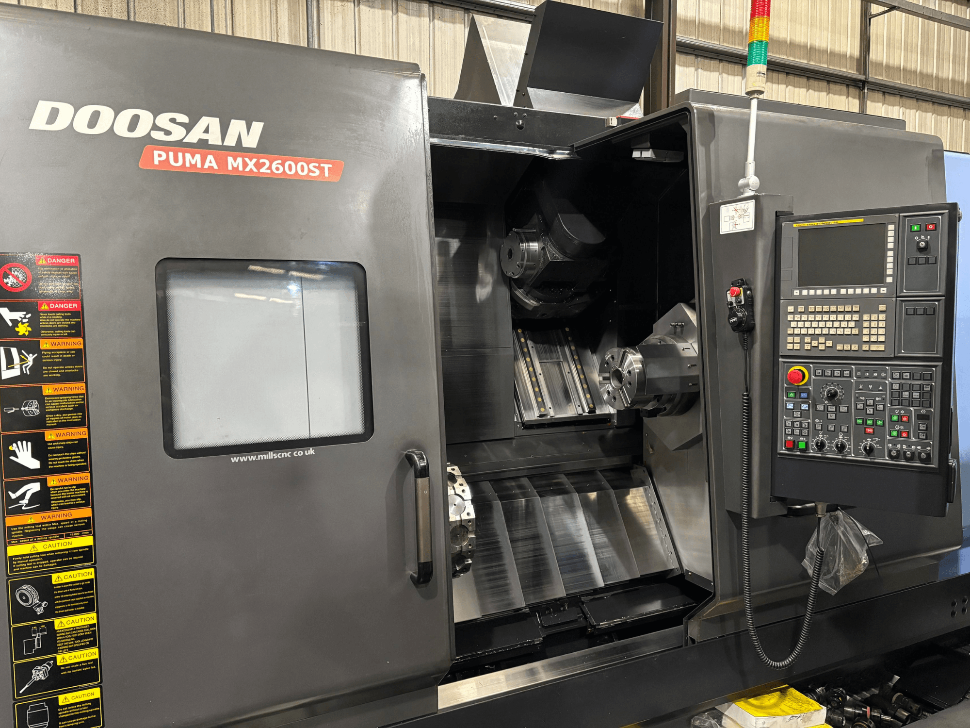 Doosan PUMA MX2600ST CNC draaibank, vooraanzicht, met het bedieningspaneel, de spindel en het bewerkingsgebied met zichtbare veiligheidswaarschuwingen.