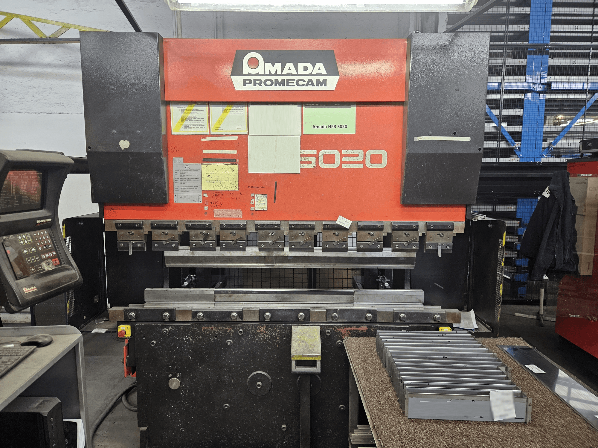 Amada HFBO 5020 afkantpers in vooraanzicht, met bedieningspaneel en gestapelde metalen onderdelen op het werkvlak.
