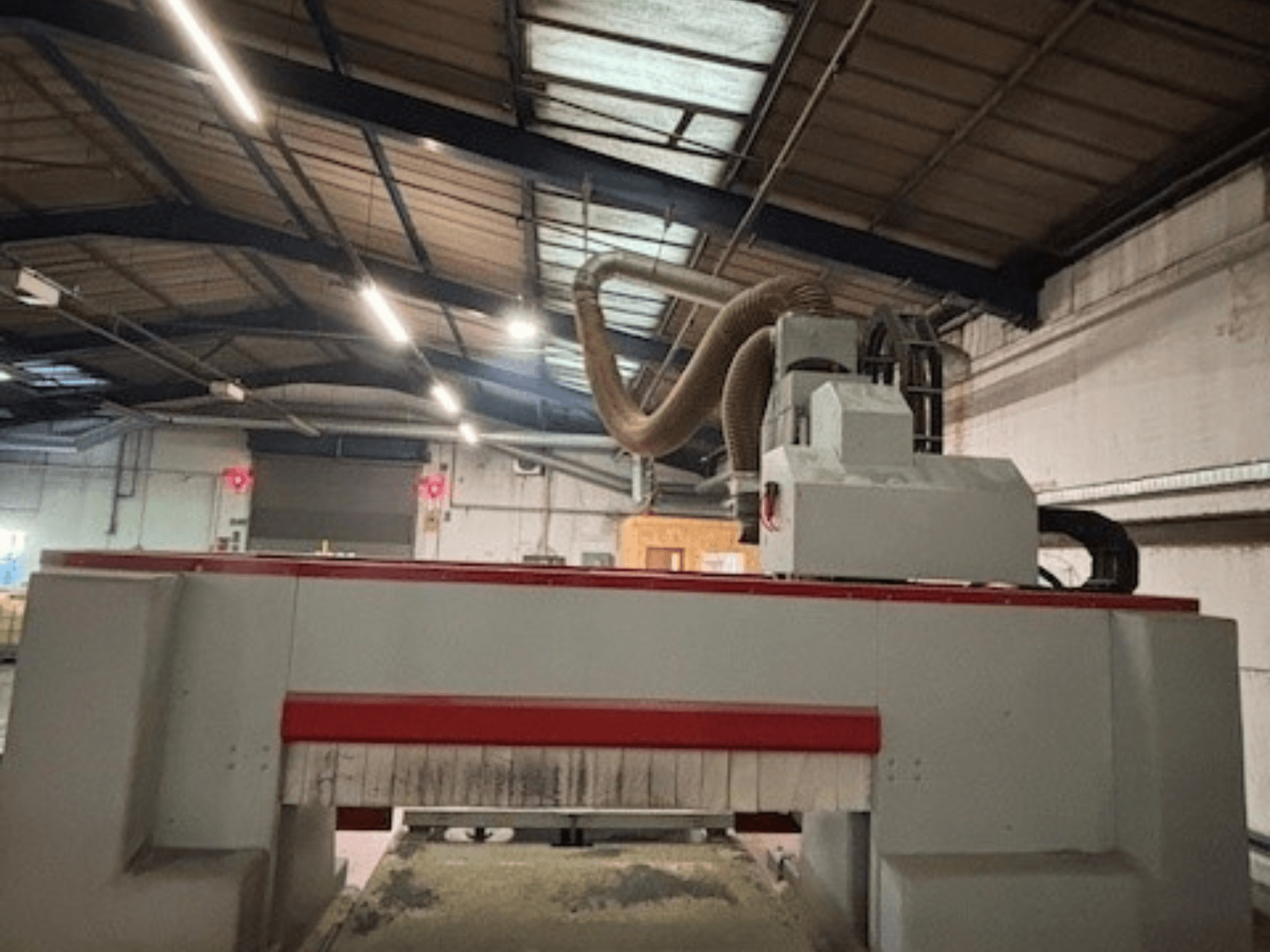 CNC bovenfreesmachine in een werkplaats, zijaanzicht met het rode en grijze ontwerp, stofafzuigsysteem bevestigd.