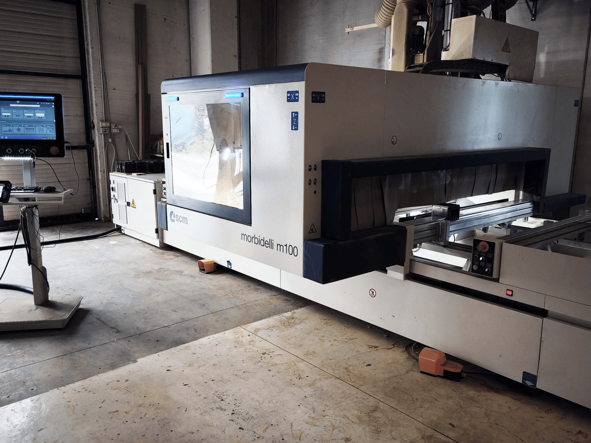 SCM Morbidelli M 100 CNC-houtbewerkingscentrum in zijaanzicht, met het bedieningspaneel, het werkgebied en de veiligheidsvoorzieningen.