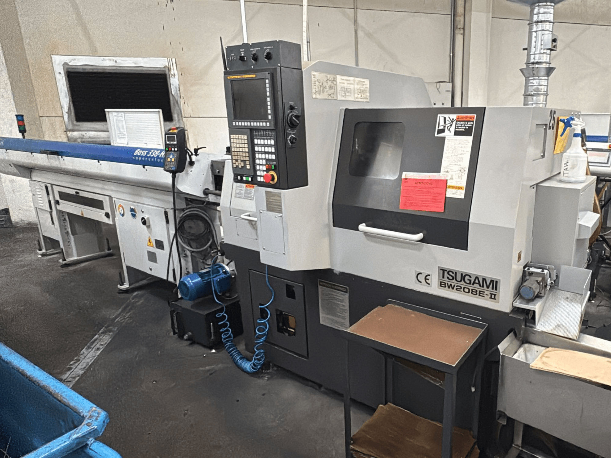 Tsugami BW208E-II CNC machine in een werkplaats, van voren gezien, met bedieningspaneel en veiligheidslabels zichtbaar.