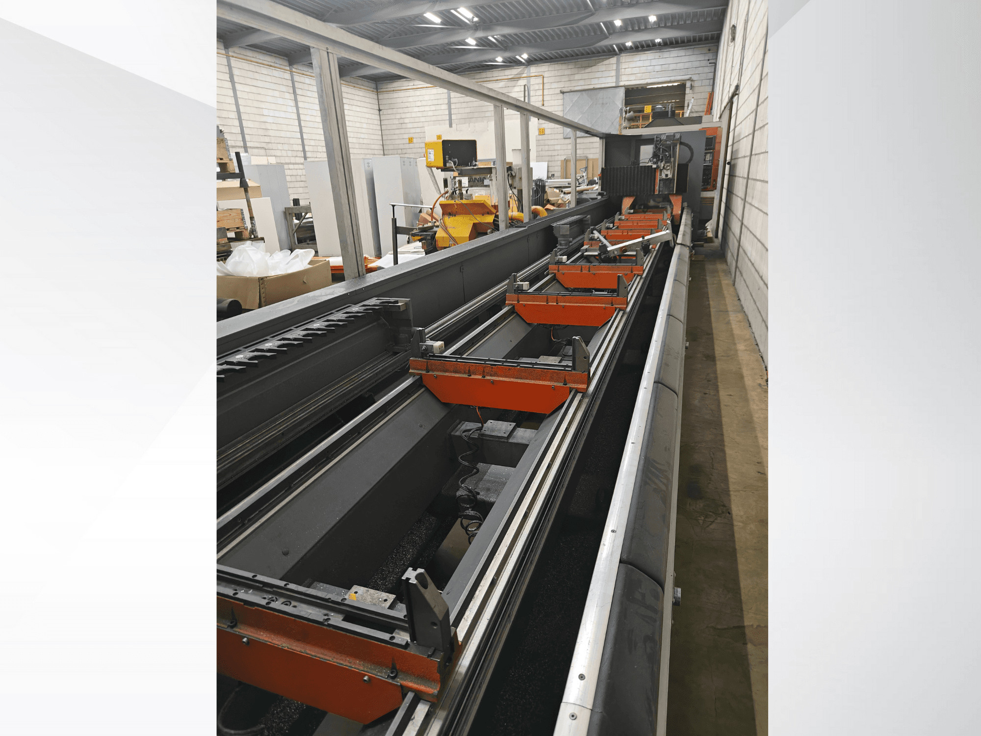 Zijaanzicht van industriële CNC machine, met lineaire rails, oranje klemmen en precisiecomponenten in een magazijnomgeving.