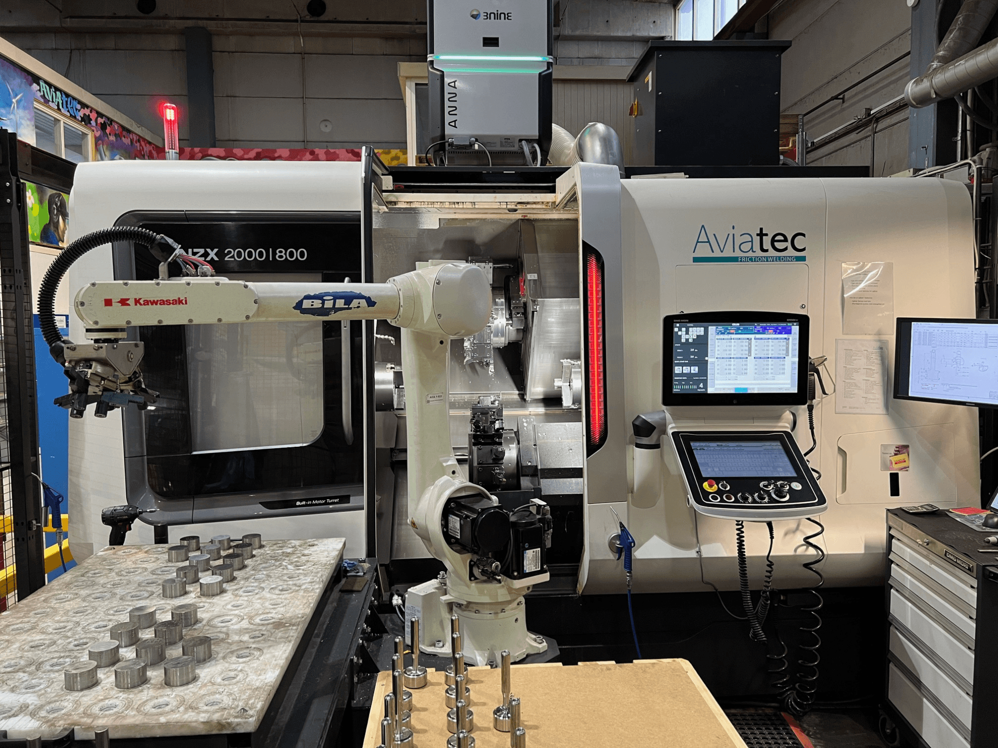 Horizontale draaibank DMG MORI NZX 2000/800SY met Kawasaki-robotarm, bedieningspaneel en metalen onderdelen op de werktafel.