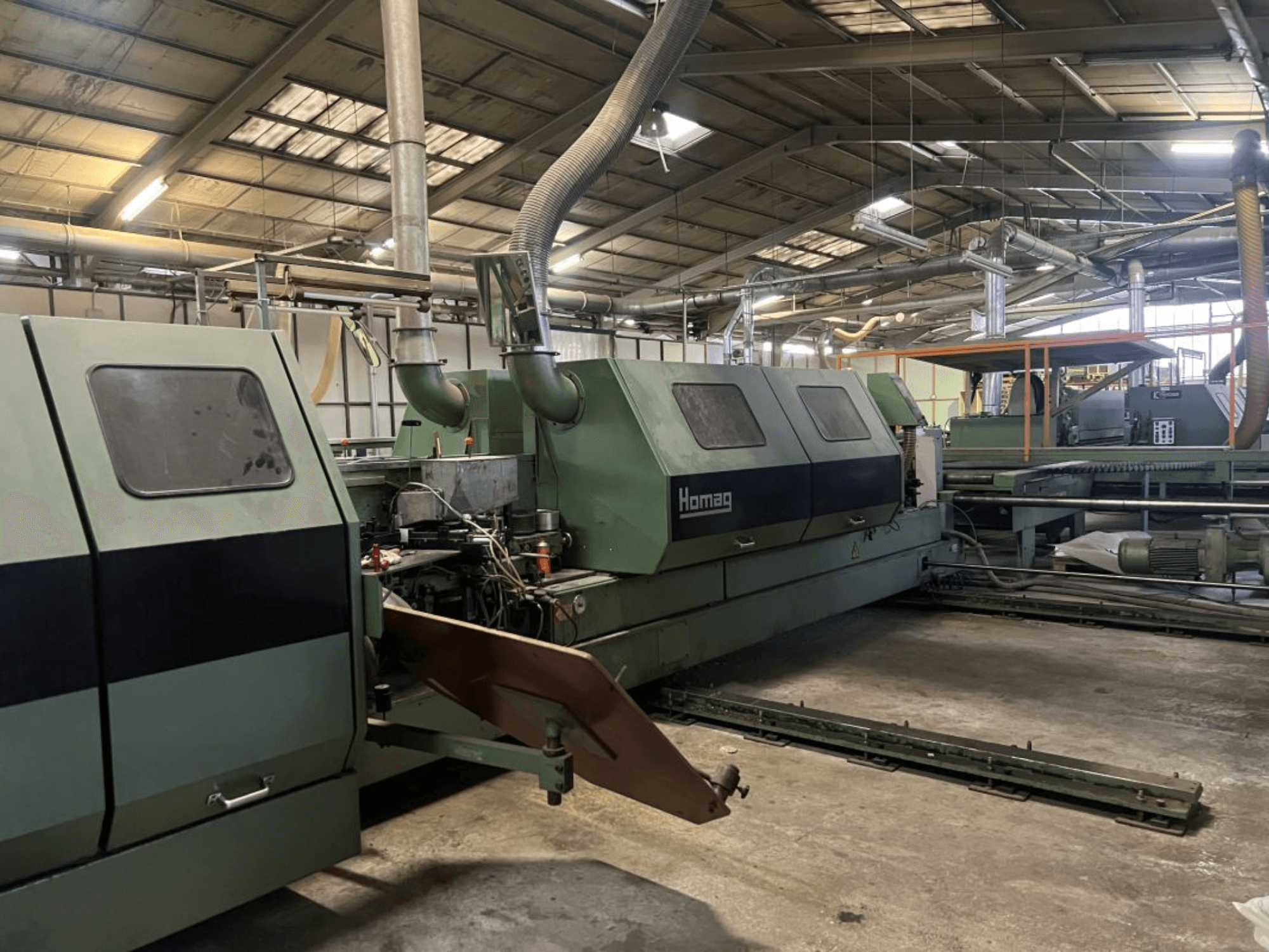 Homag industriële machine in groen, zijaanzicht, met operationele onderdelen en bedieningspaneel zichtbaar in een magazijn.