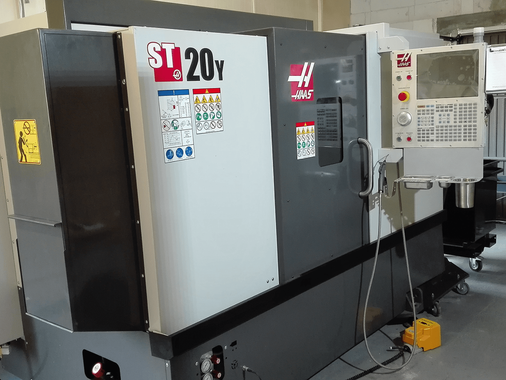 Haas ST20Y CNC draaibank in vooraanzicht, met bedieningspaneel, veiligheidslabels en koelvloeistofsysteem.