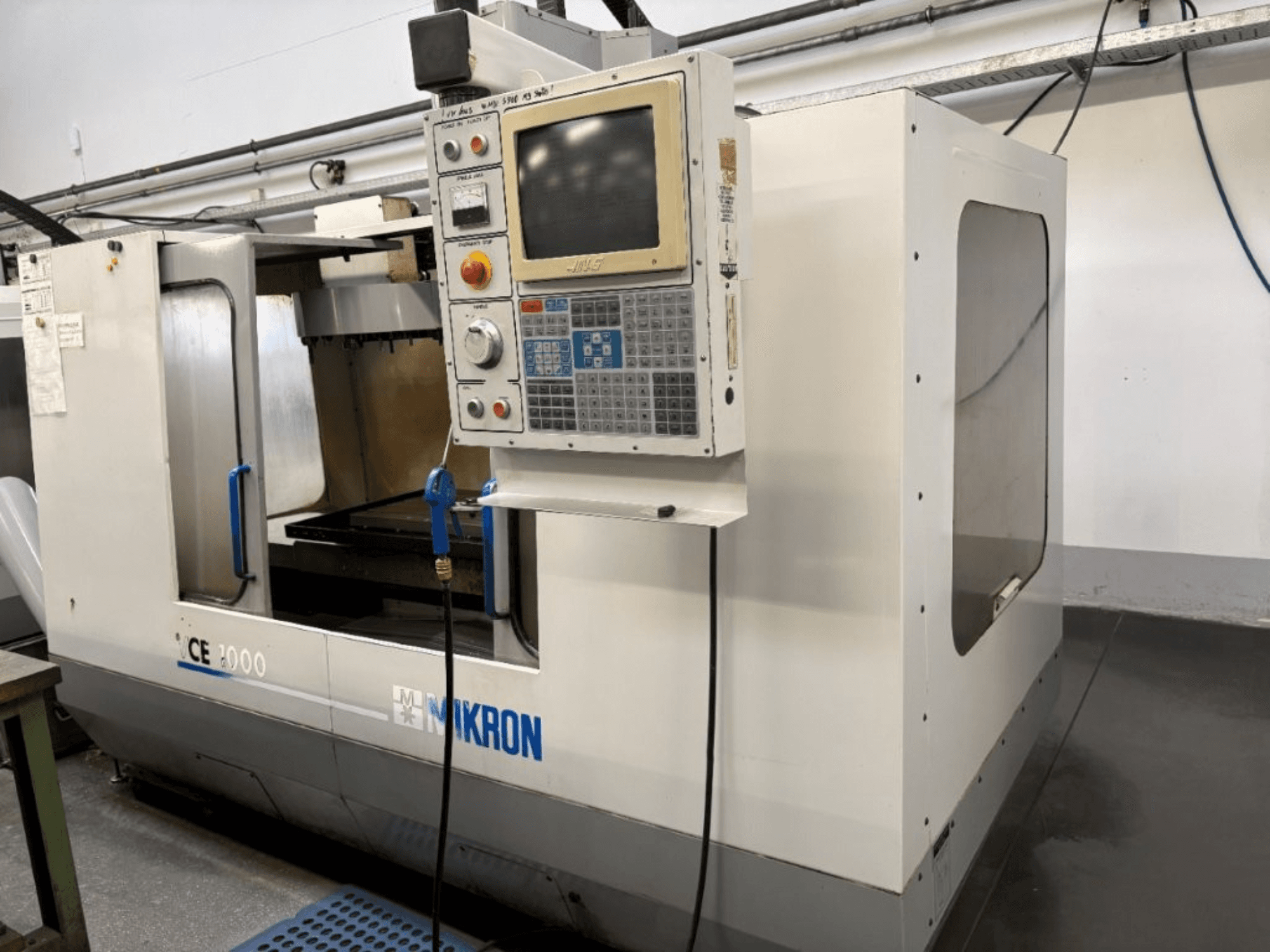 Mikron CE 2000 CNC machine, vooraanzicht; heeft een bedieningspaneel met knoppen en scherm, zilveren buitenkant, en werkgebied.