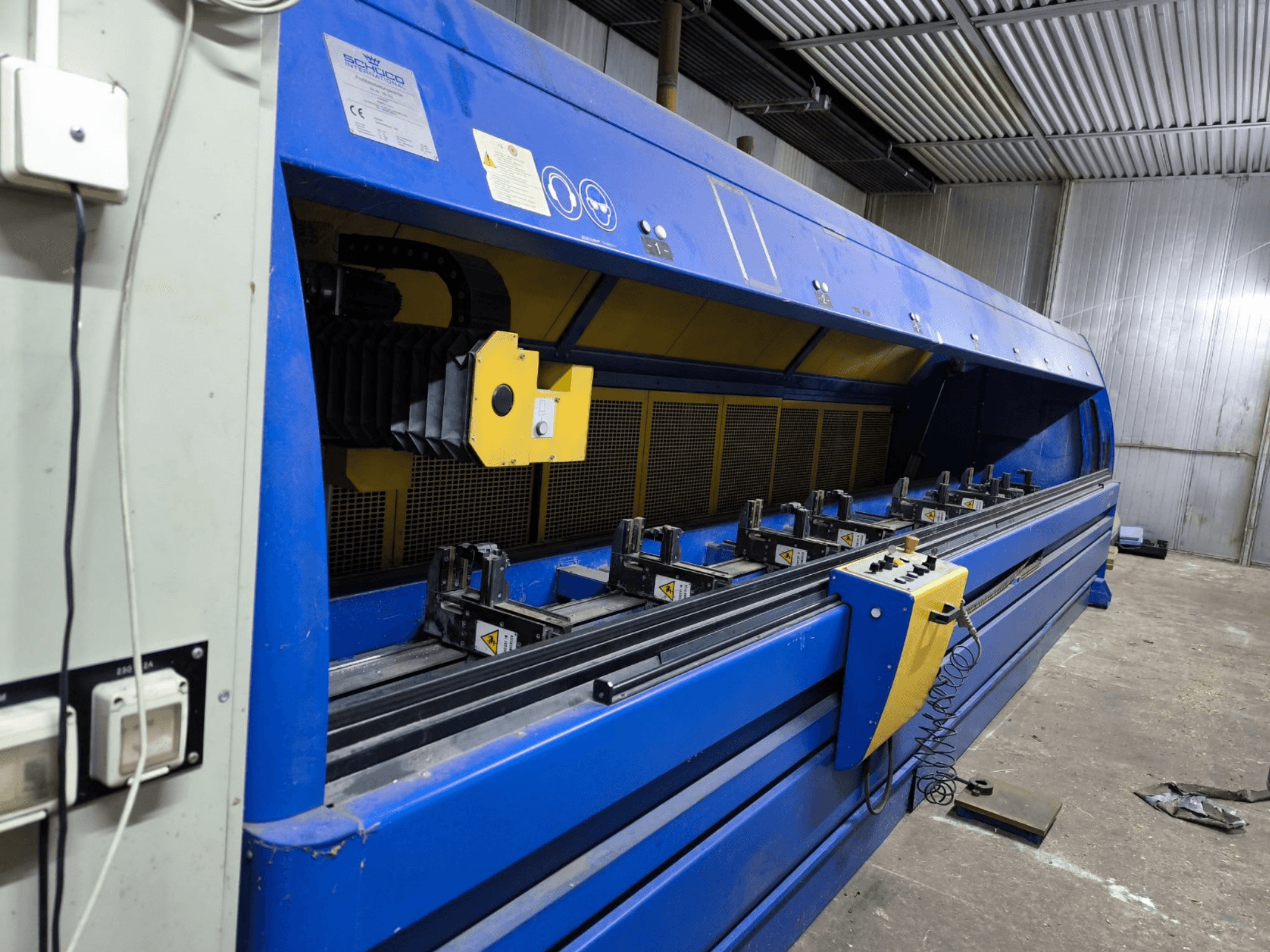 Schneider industriële snijmachine in blauw, zijaanzicht, met bedieningspaneel, riemen en meerdere opspanstations zichtbaar.