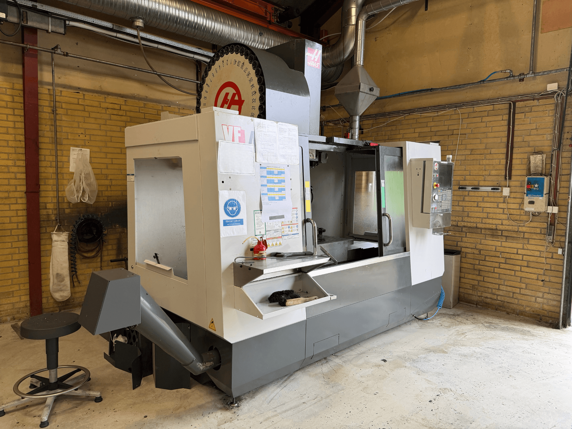 HAAS VF-4 verticaal bewerkingscentrum, vooraanzicht; met bedieningspaneel, gereedschapshouder en productieopstelling op de achtergrond.