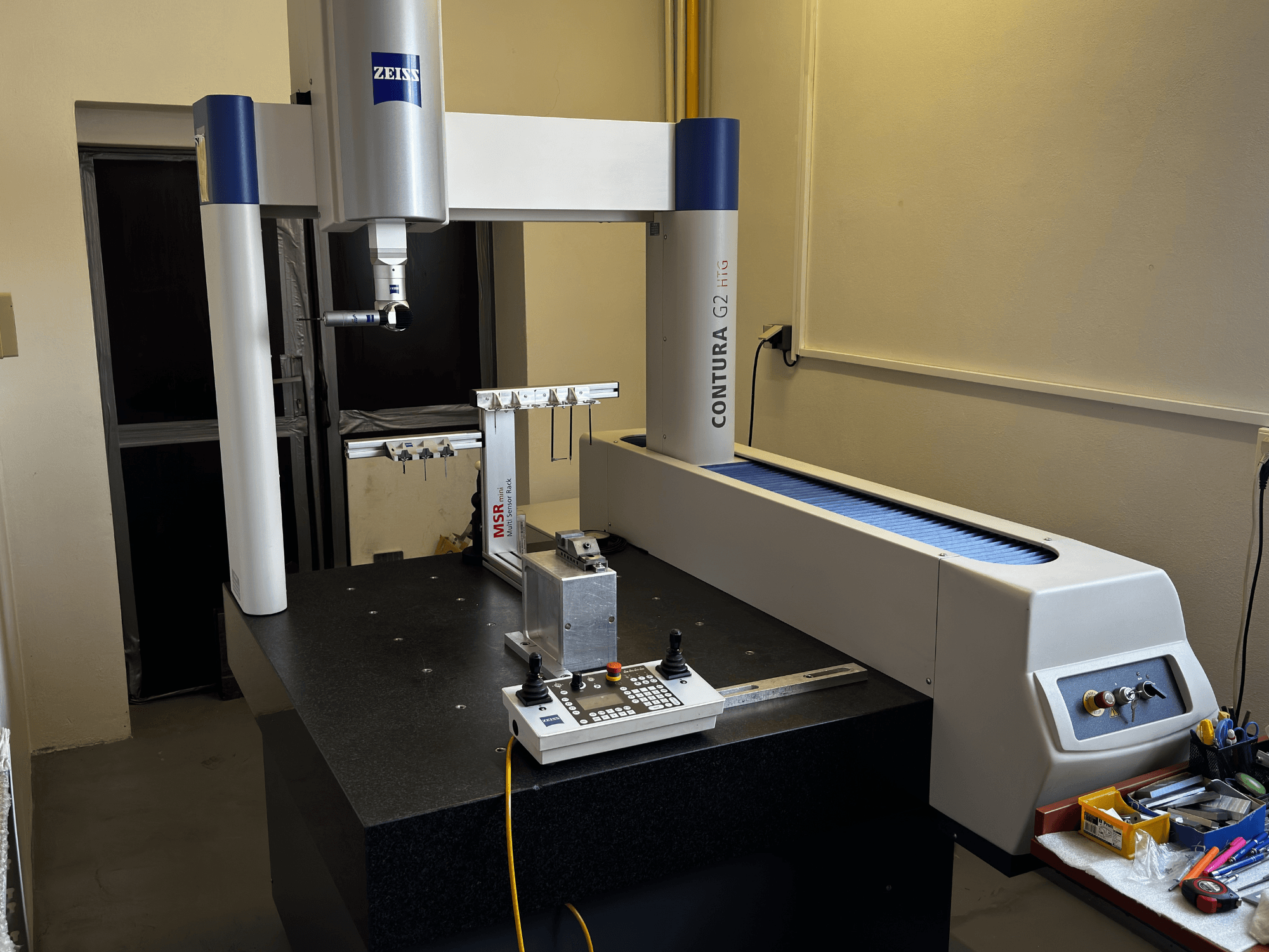 ZEISS Contura G2 CMM in een laboratoriumomgeving, vooraanzicht met meetarm, bedieningspaneel en aangrenzende werkruimte.