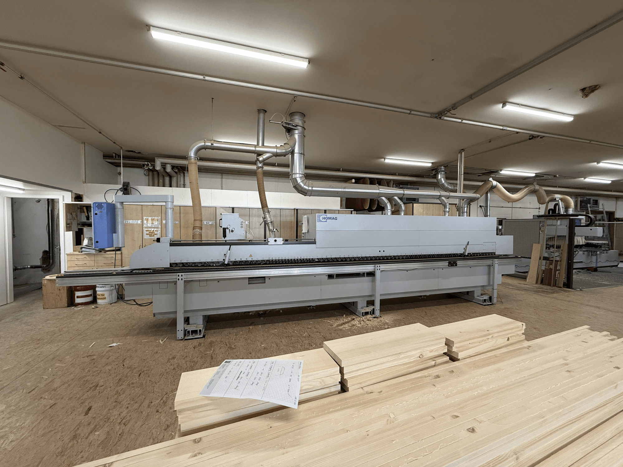 HOMAG KAL211 kantenbewerker in een werkplaats, vooraanzicht, met houten planken en machines in een goed verlichte omgeving.