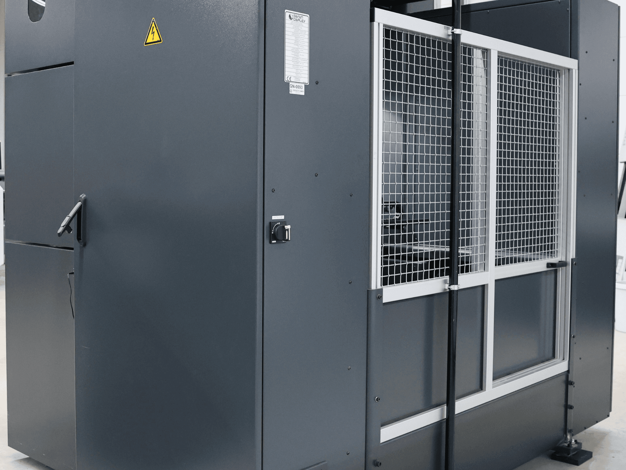 Grijze industriële machine met veiligheidswaarschuwing, vooraanzicht met gaasdeur en bedieningspaneel, model gelabeld.