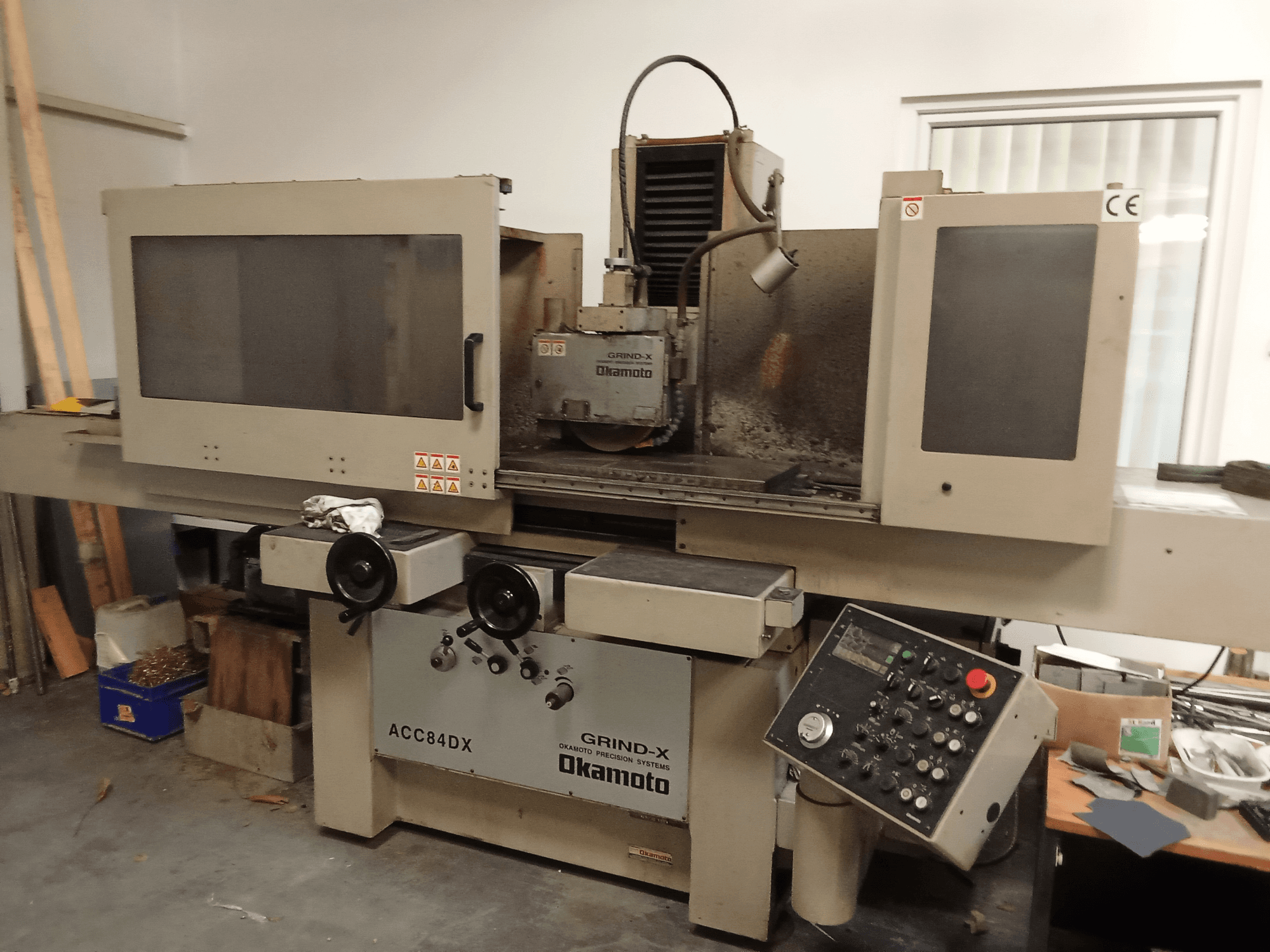 Vooraanzicht van de OKAMOTO ACC84 DX-vlakschuurmachine, met bedieningspaneel en afscherming van de slijpschijf.