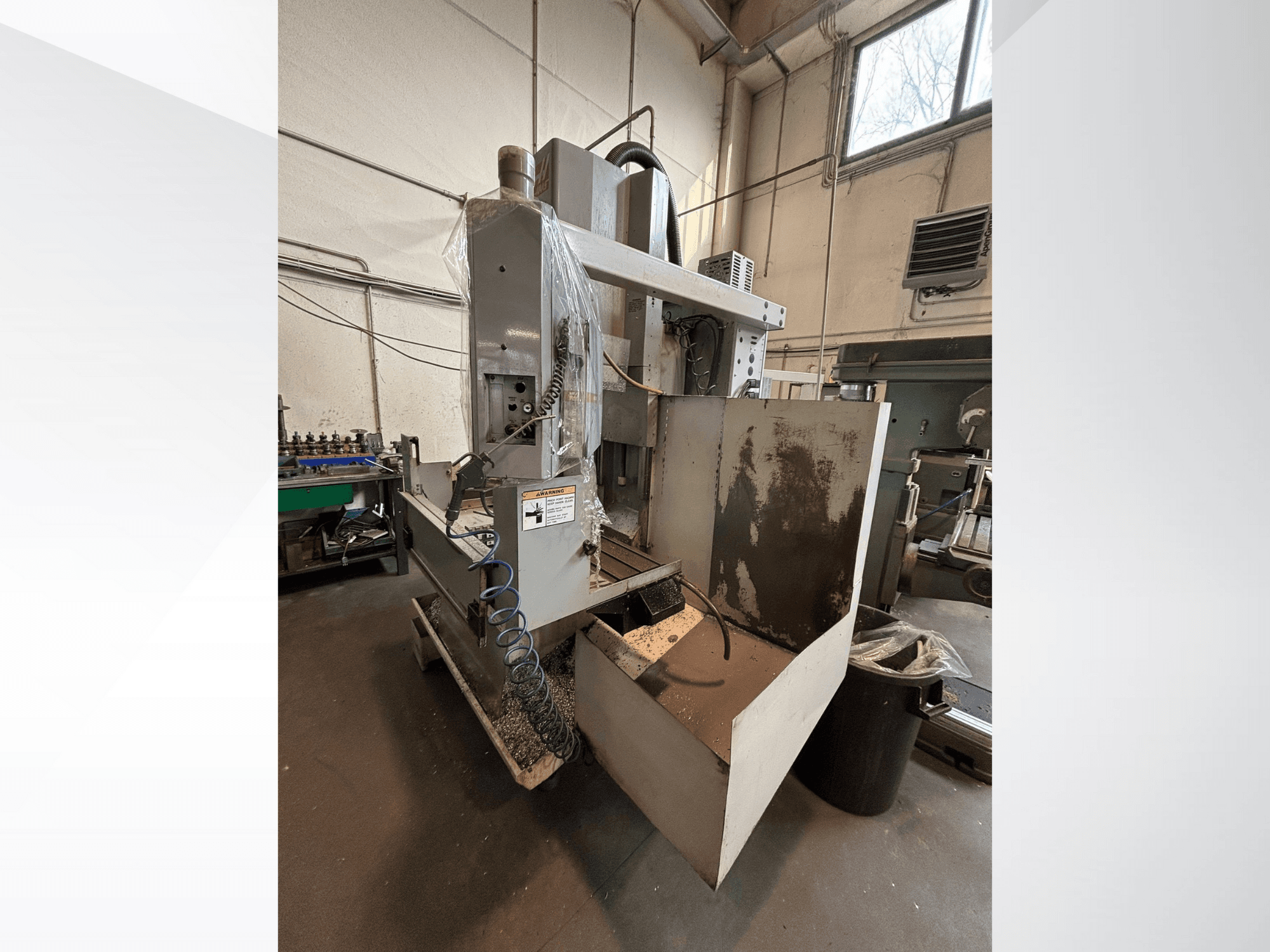 Verticale freesmachine met beschermkap, zijaanzicht; inclusief koelslang en bedieningspaneel zichtbaar. Ideaal voor machinale bewerking.