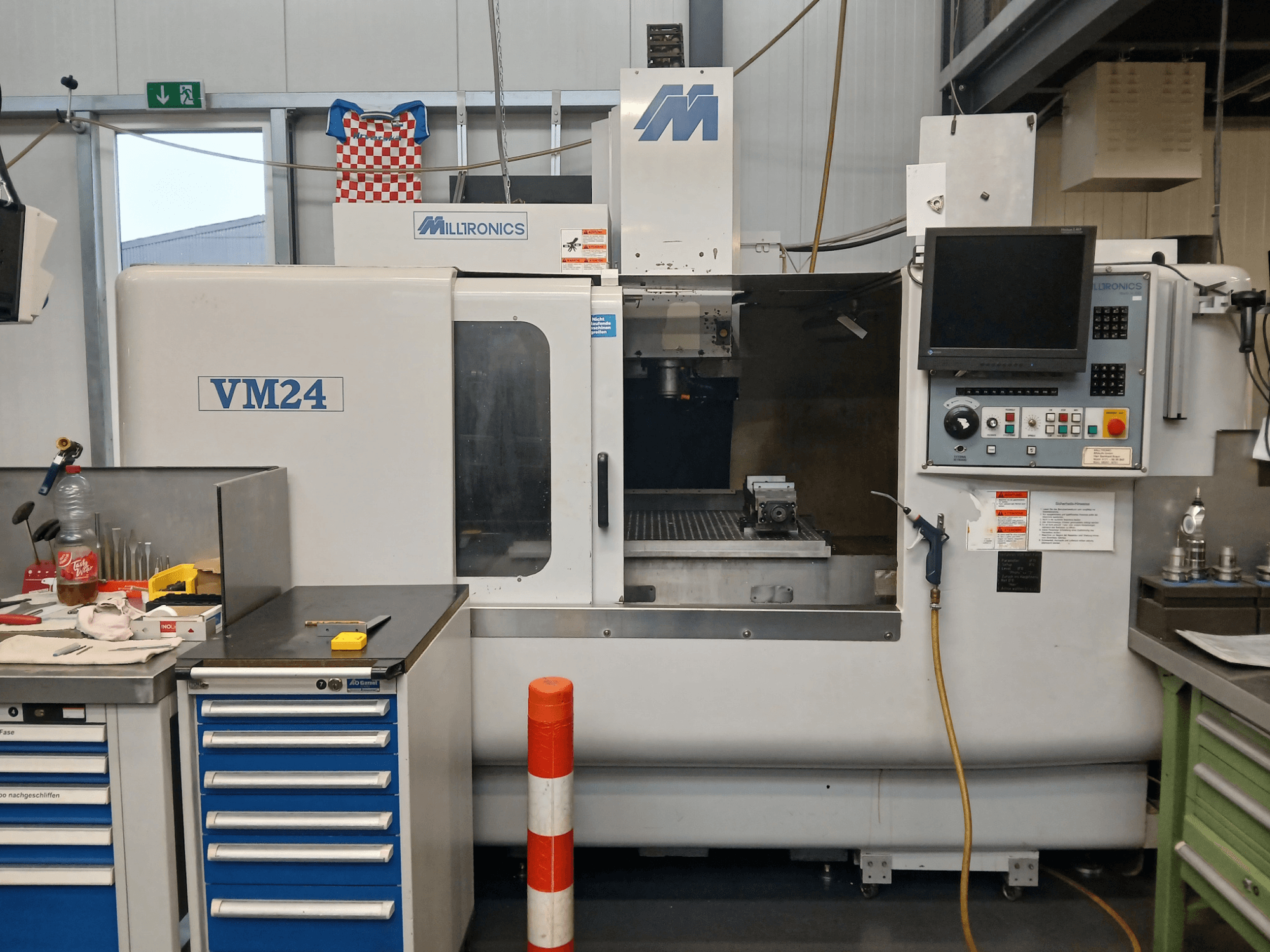 Milltronics VM24 CNC freesmachine getoond vanaf de voorkant, met bedieningspaneel, gereedschapopslag en werkgebiedopstelling.