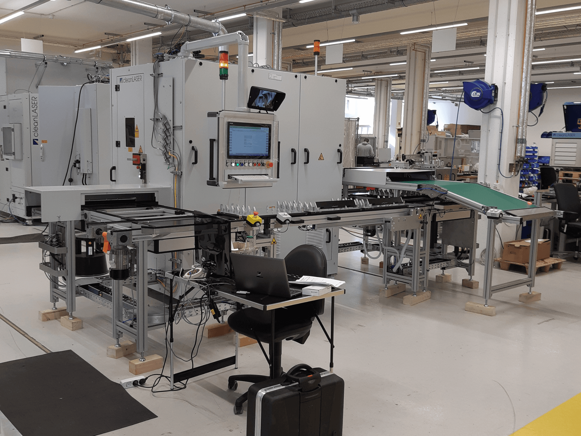 CLEAN LASER clean CELL 3220-bewerkingsmachine, vooraanzicht met het bedieningspaneel, de transportband en de werkruimteopstelling in een fabrieksomgeving.
