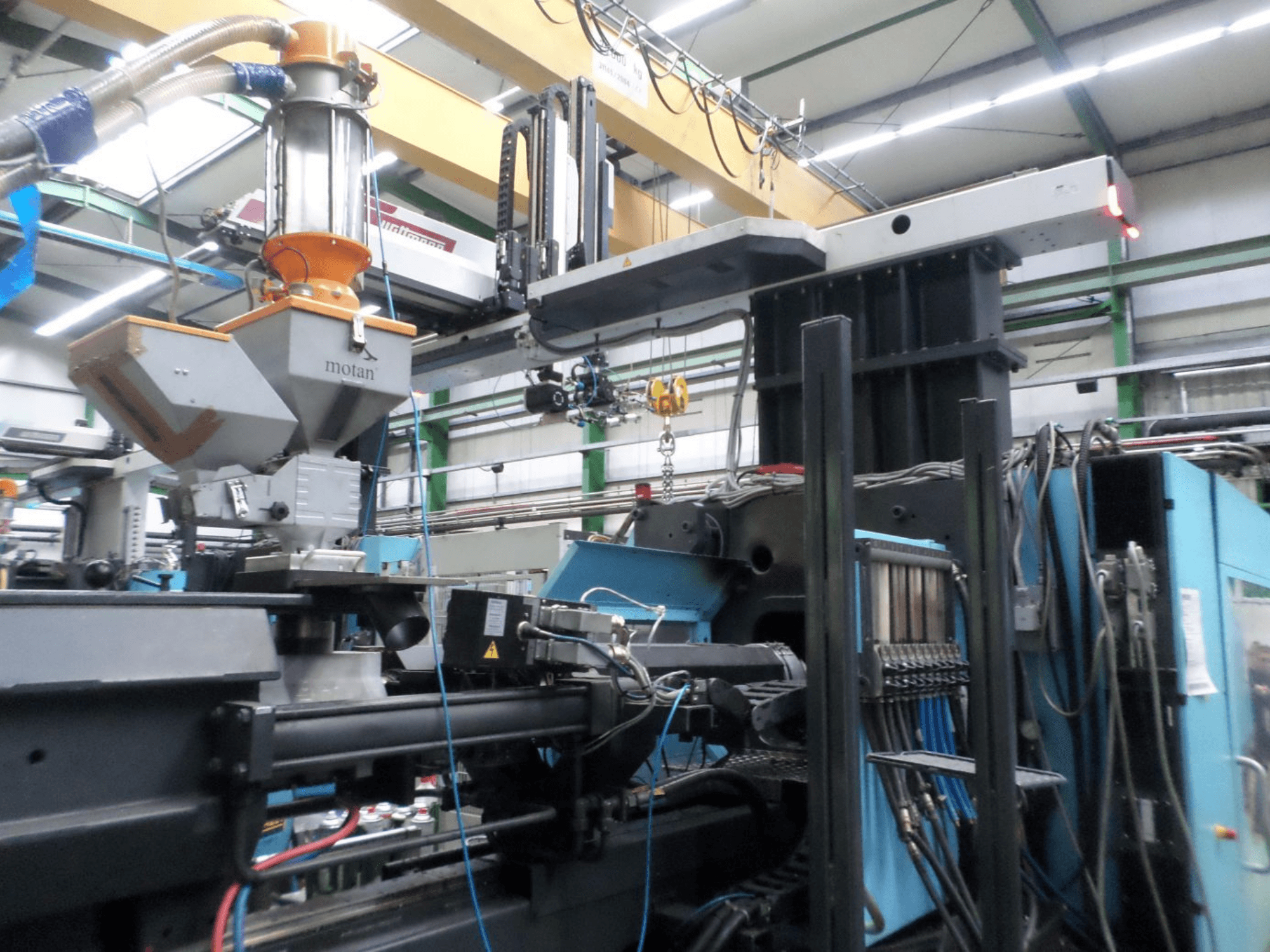 Hydraulische spuitgietmachine DEMAG D 1300, zijaanzicht, met weergave van de trechter, de besturingseenheid en de aansluitingen in een fabrieksomgeving.
