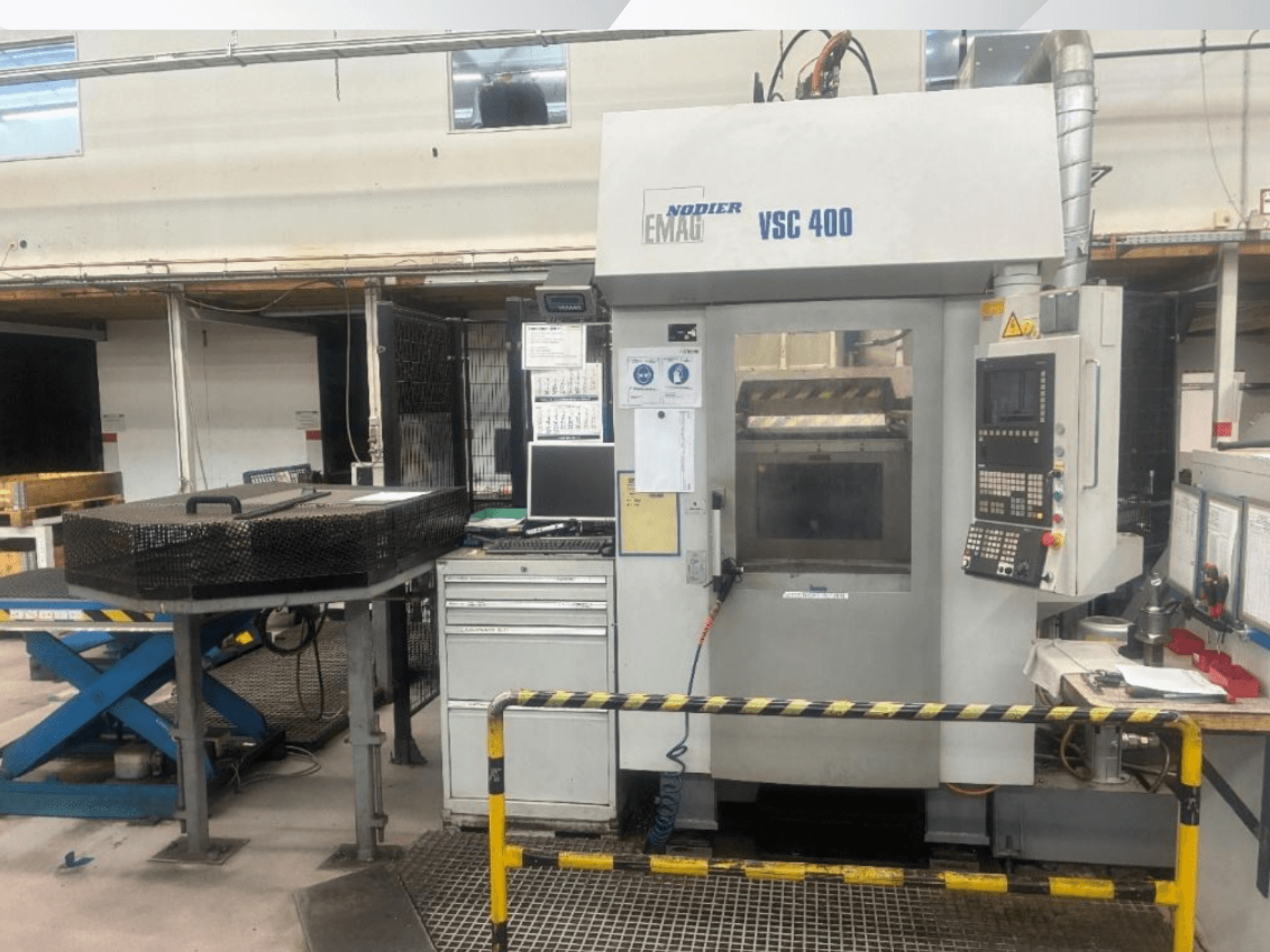 Vooraanzicht van de verticale draaimachine EMAG VSC 400, met bedieningspaneel, veiligheidshekken en omliggende apparatuur in een goed verlichte werkplaats.