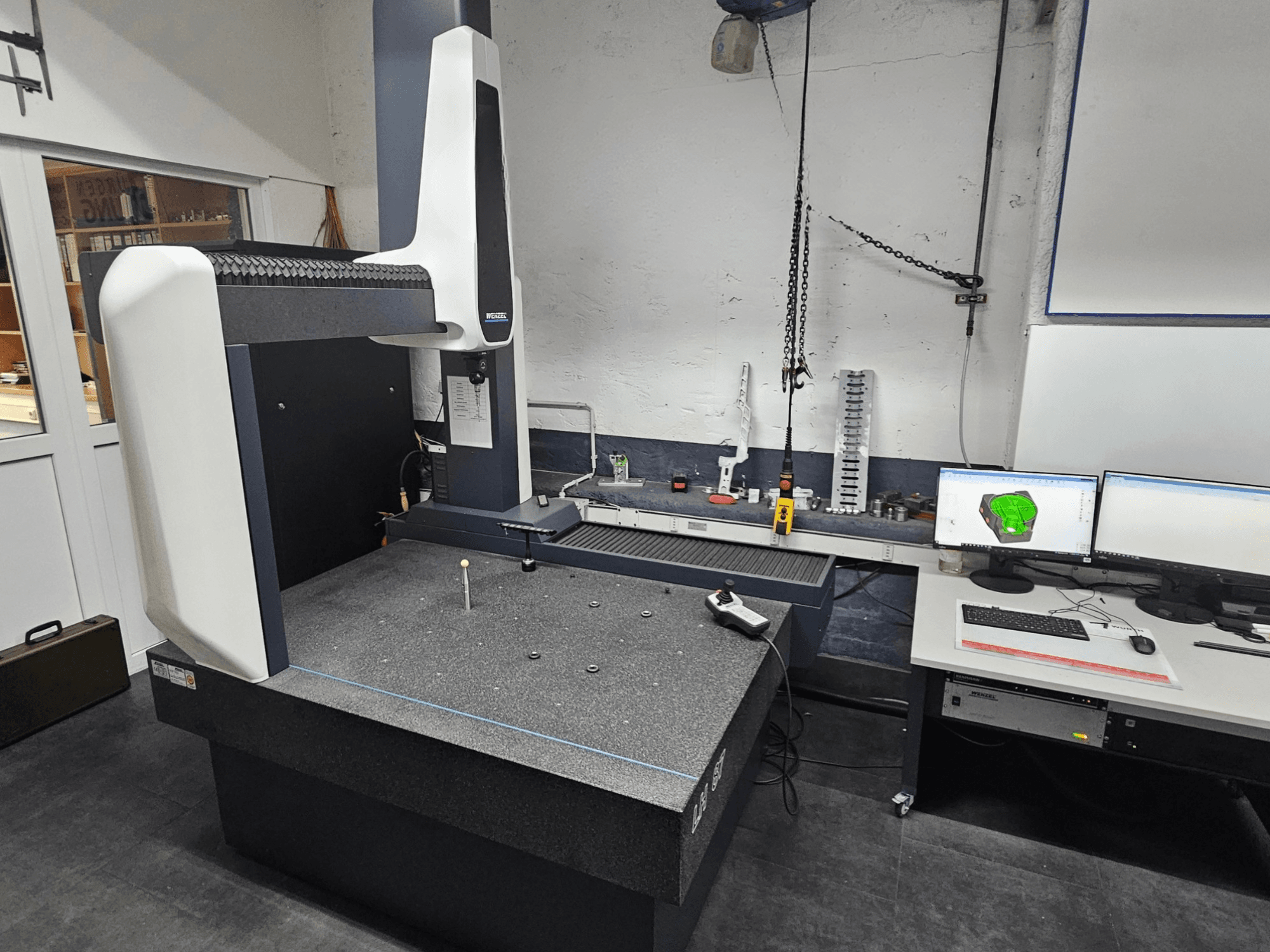 Coördinatenmeetmachine Wenzel LH 87 in een werkplaats, vooraanzicht, met een taster op de graniettafel en twee monitoren die het CAD-ontwerp weergeven.
