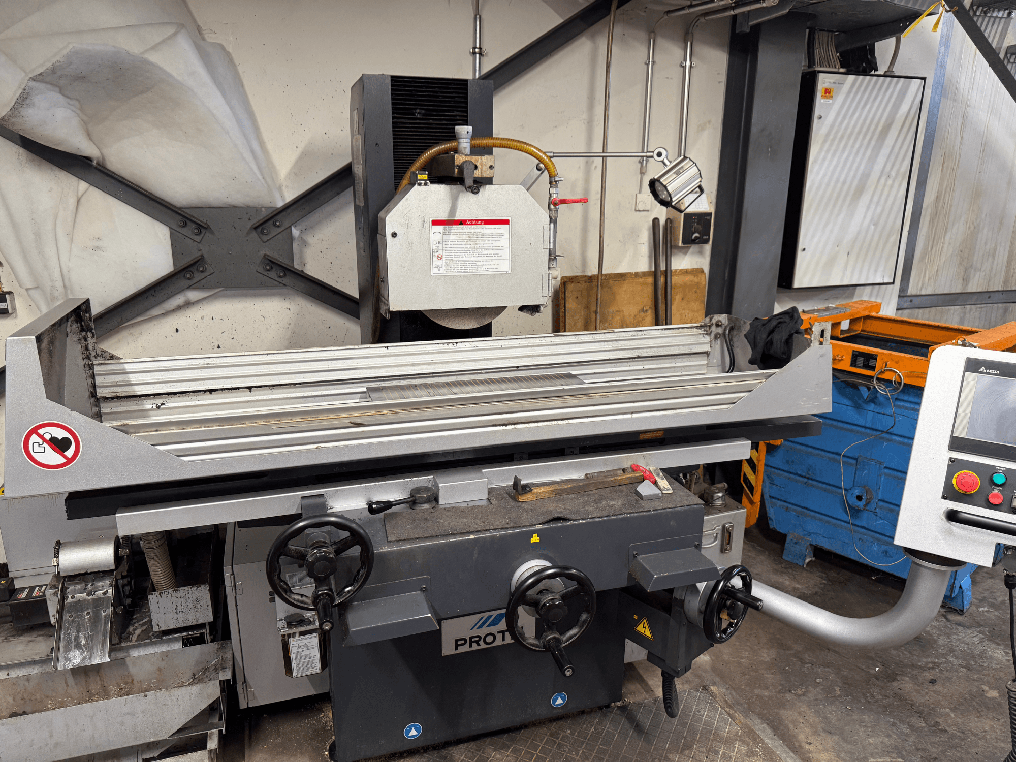 PROTEC machine, vooraanzicht, toont een vlakslijpmachine met handbediening, veiligheidswaarschuwingen en een koelsysteem.