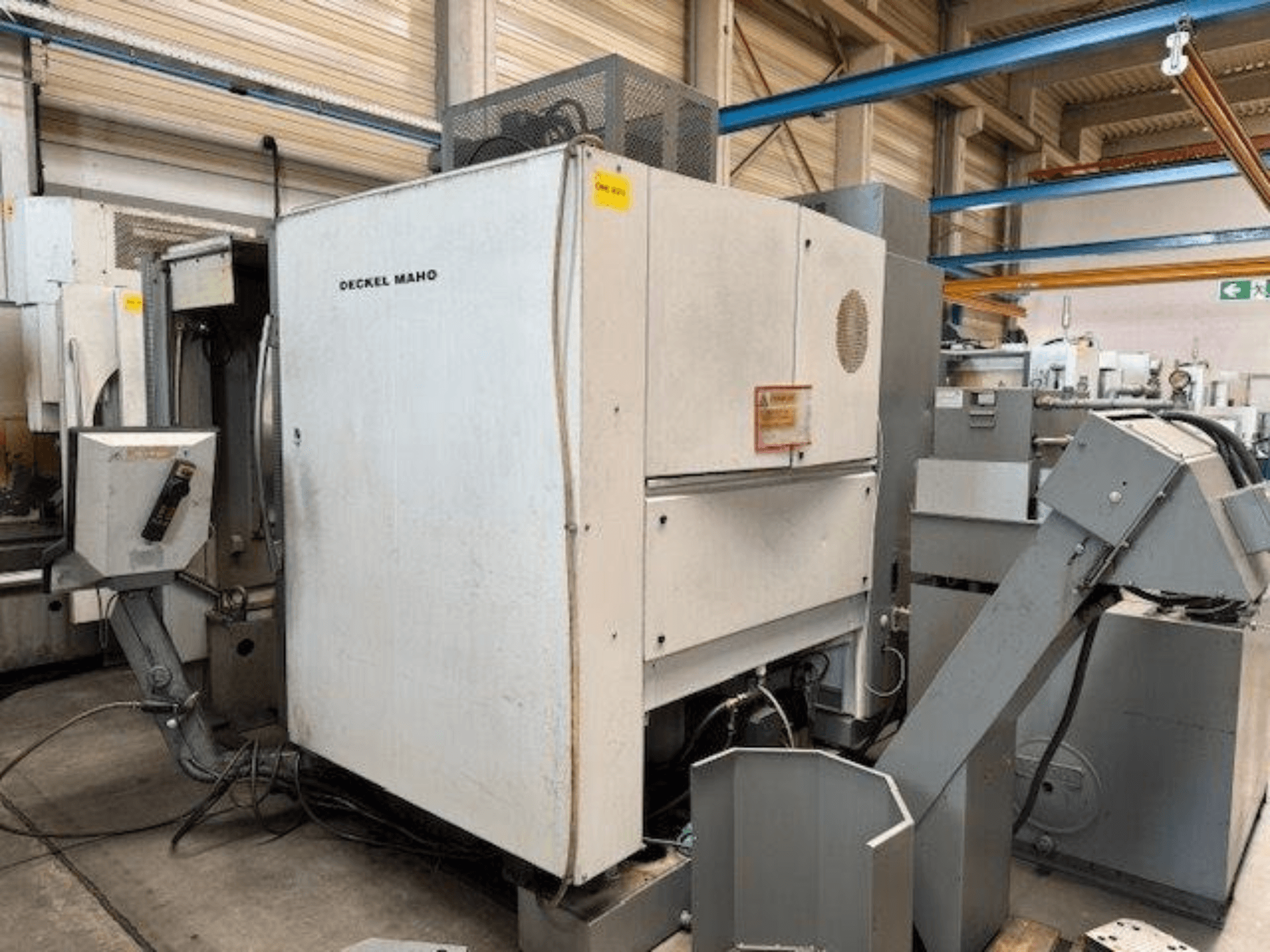 DECKEL MAHO DMC 100 V verticaal bewerkingscentrum, zijaanzicht met bedieningspaneel en diverse hulpstukken zichtbaar.