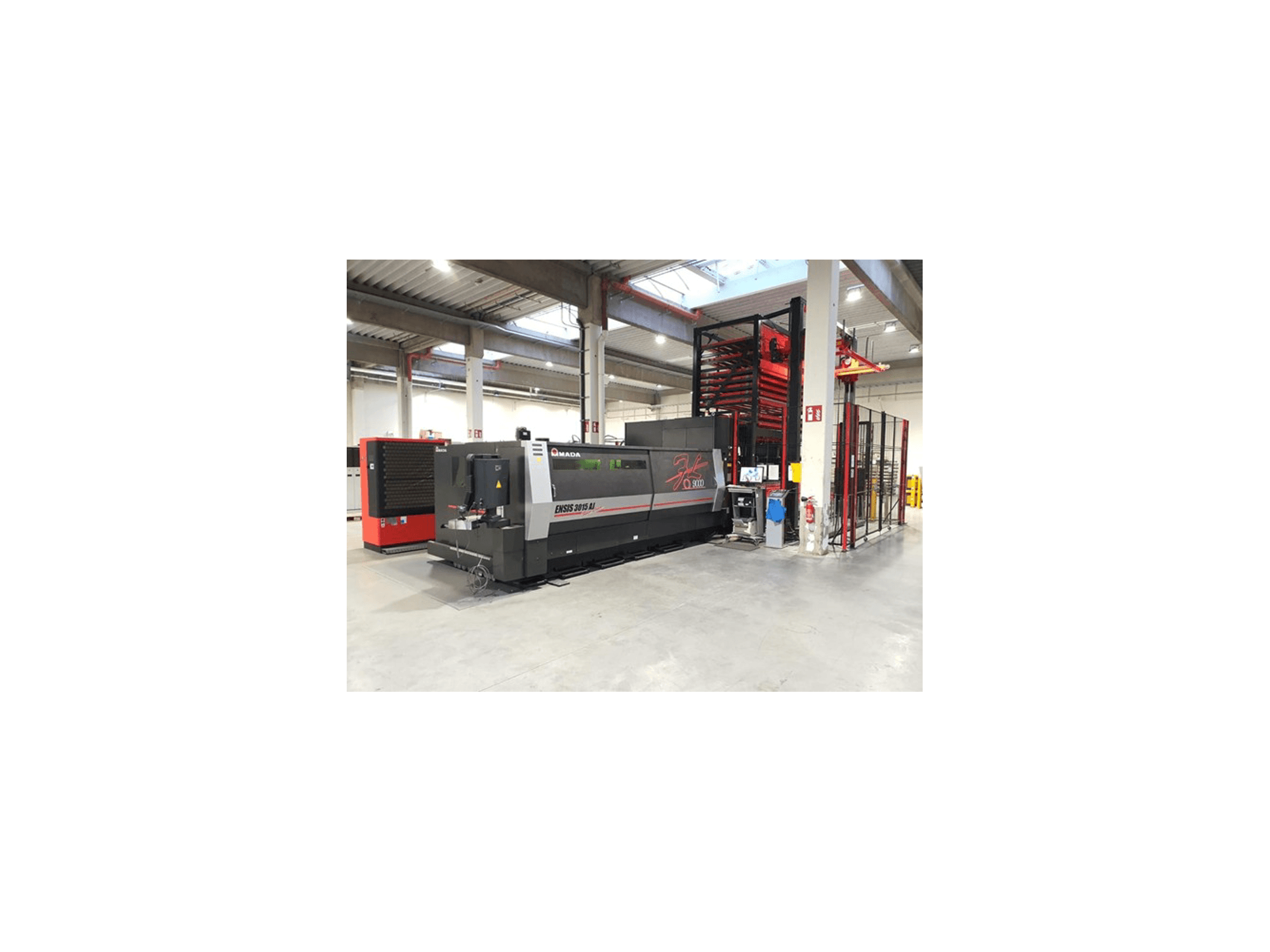 Amada ENSIS 3015 Aj lasersnijmachine in vooraanzicht, opgesteld in een ruime industriële werkplaats met metalen rekken.