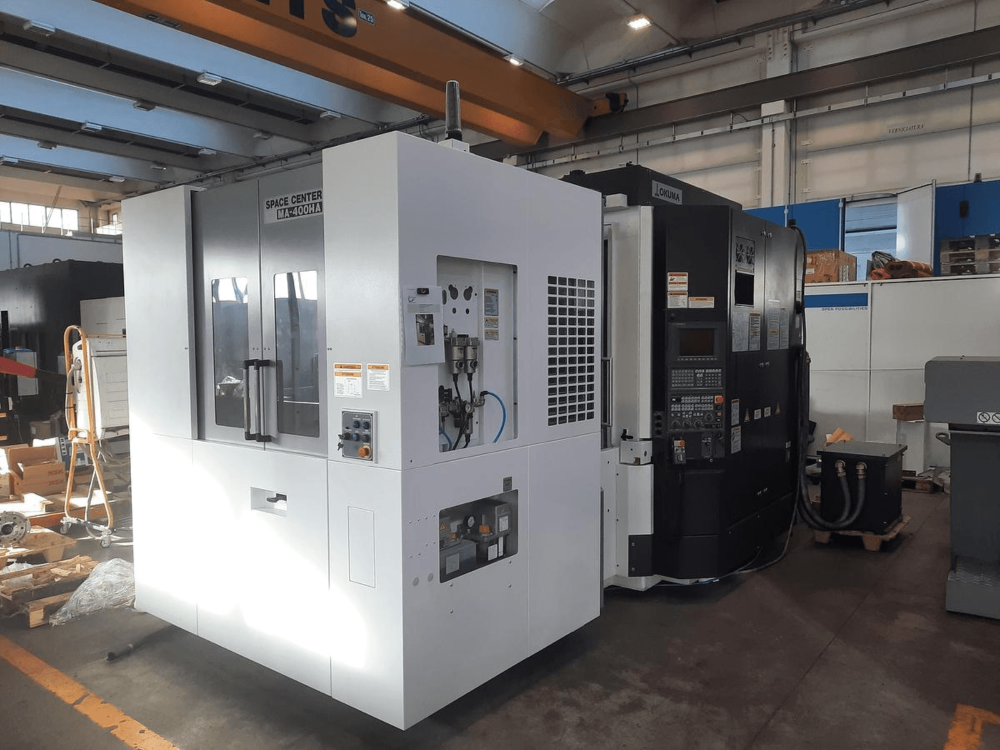 Vooraanzicht van SPACE CENTER IM-400HAA en OKUMA CNC machines, met diverse bedieningselementen en labels van de fabrikant.