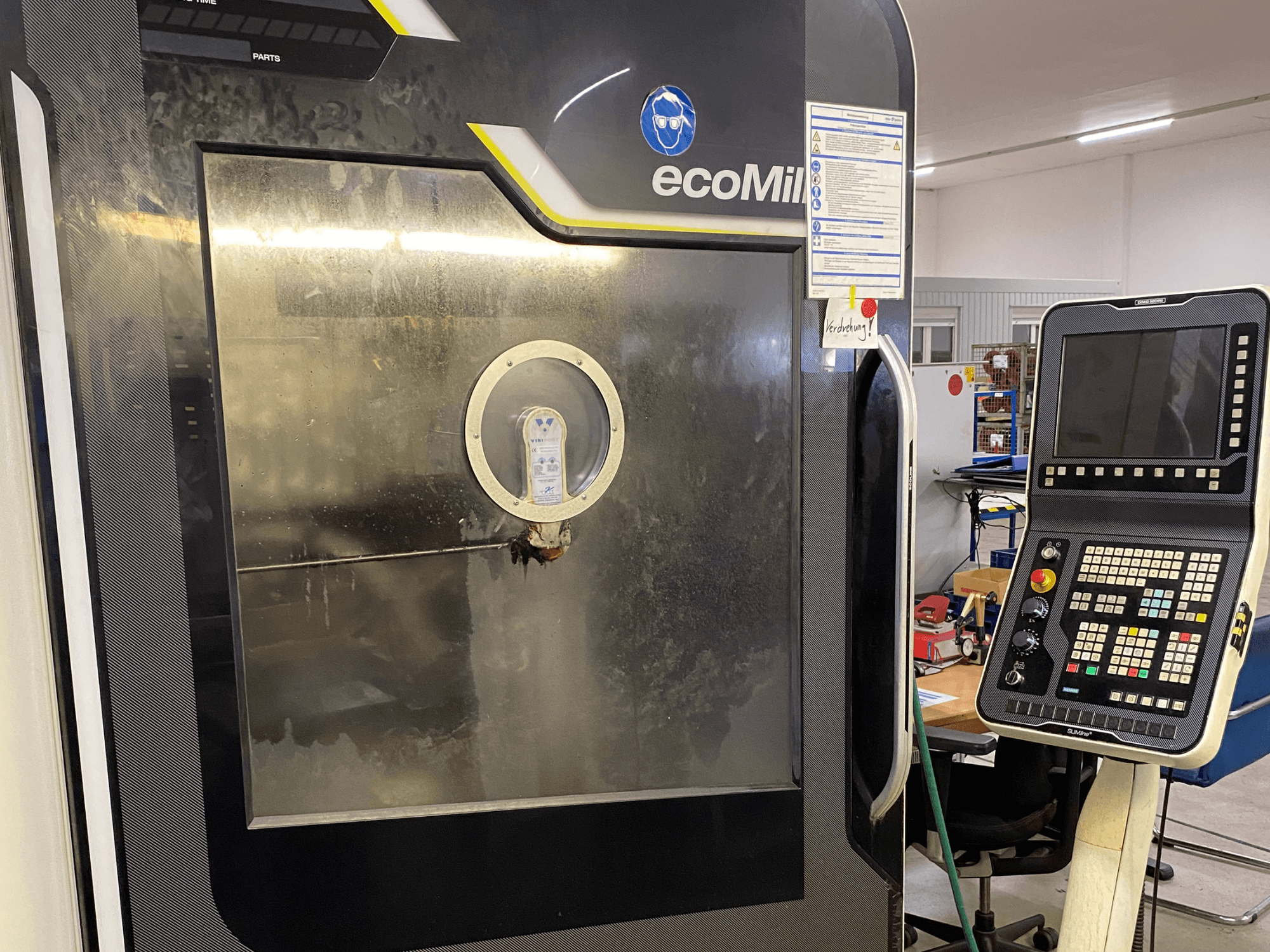 De DMG MU 70 ECO-freesmachine in vooraanzicht, met rechts een bedieningspaneel en een glazen paneel waardoor de onderdelen binnenin zichtbaar zijn.