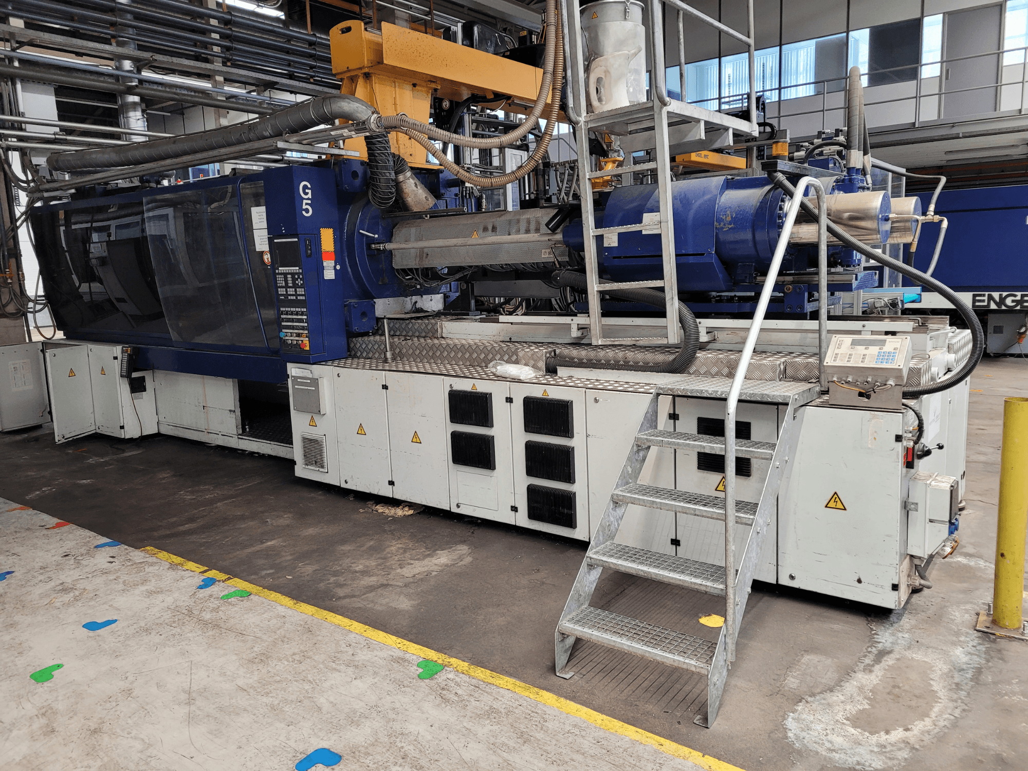 Spuitgietmachine G5, zijaanzicht, met bedieningspaneel, trapladder en roestvrijstalen werkblad zichtbaar.