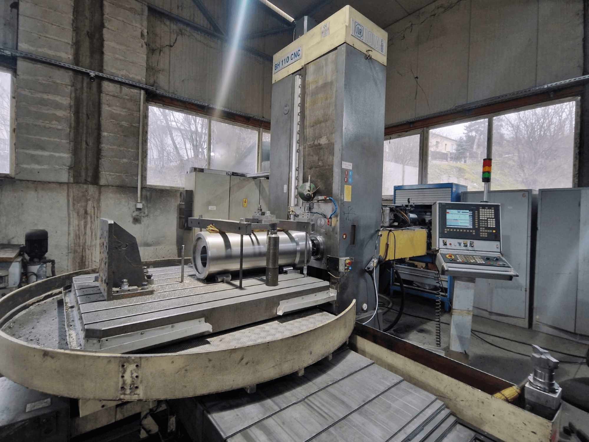 LOLA BH 110 CNC kottermachine in een werkplaats, vooraanzicht, met metalen werkstuk en bedieningspaneel.