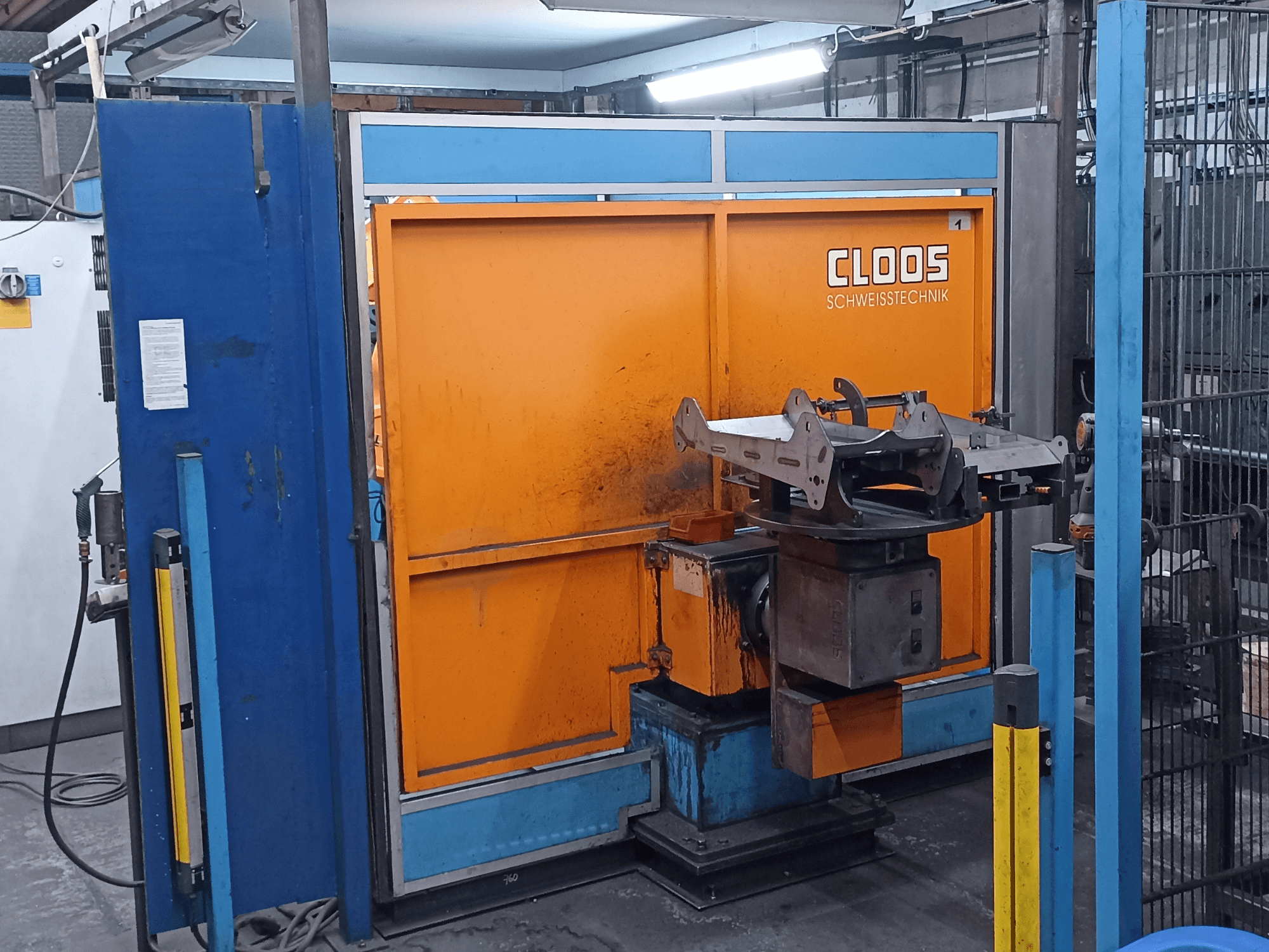 CLOOS Romat 320-lasrobot in een werkplaats, vooraanzicht, met een oranje bedieningspaneel en een metalen werkstuk op een draaibare voet.
