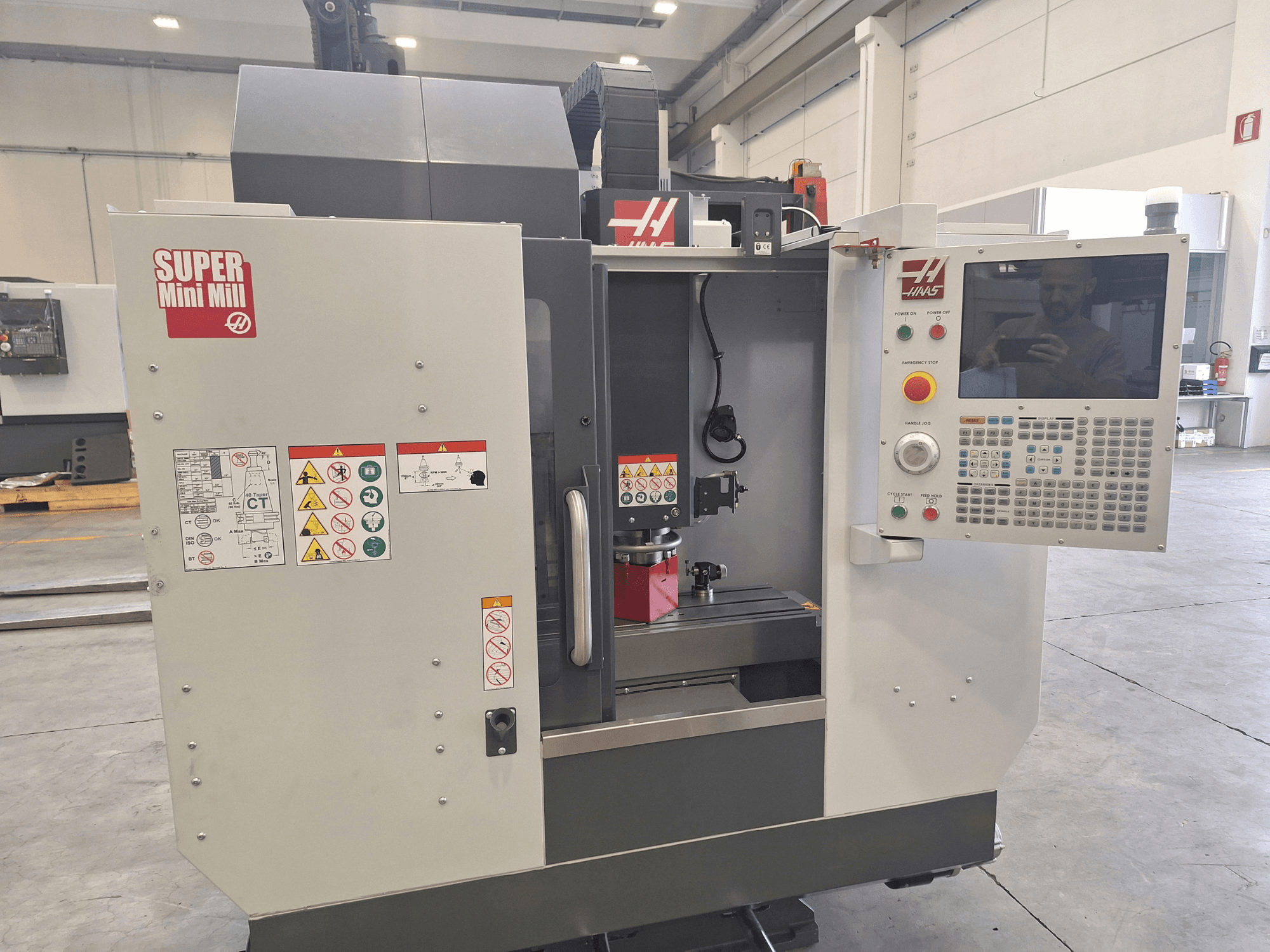 Vooraanzicht van de HAAS Super Mini Mill, met daarop het bedieningspaneel, veiligheidslabels en het bewerkingsgebied met een opgezet werkstuk.