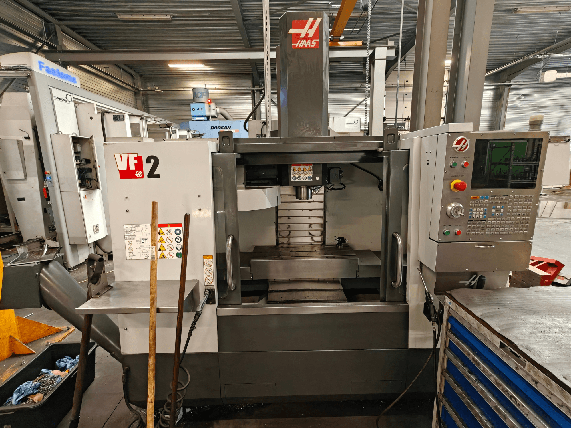 HAAS VF-2 verticaal bewerkingscentrum, vooraanzicht, met de bedieningselementen, de spil en de werktafel in een werkplaatsomgeving.