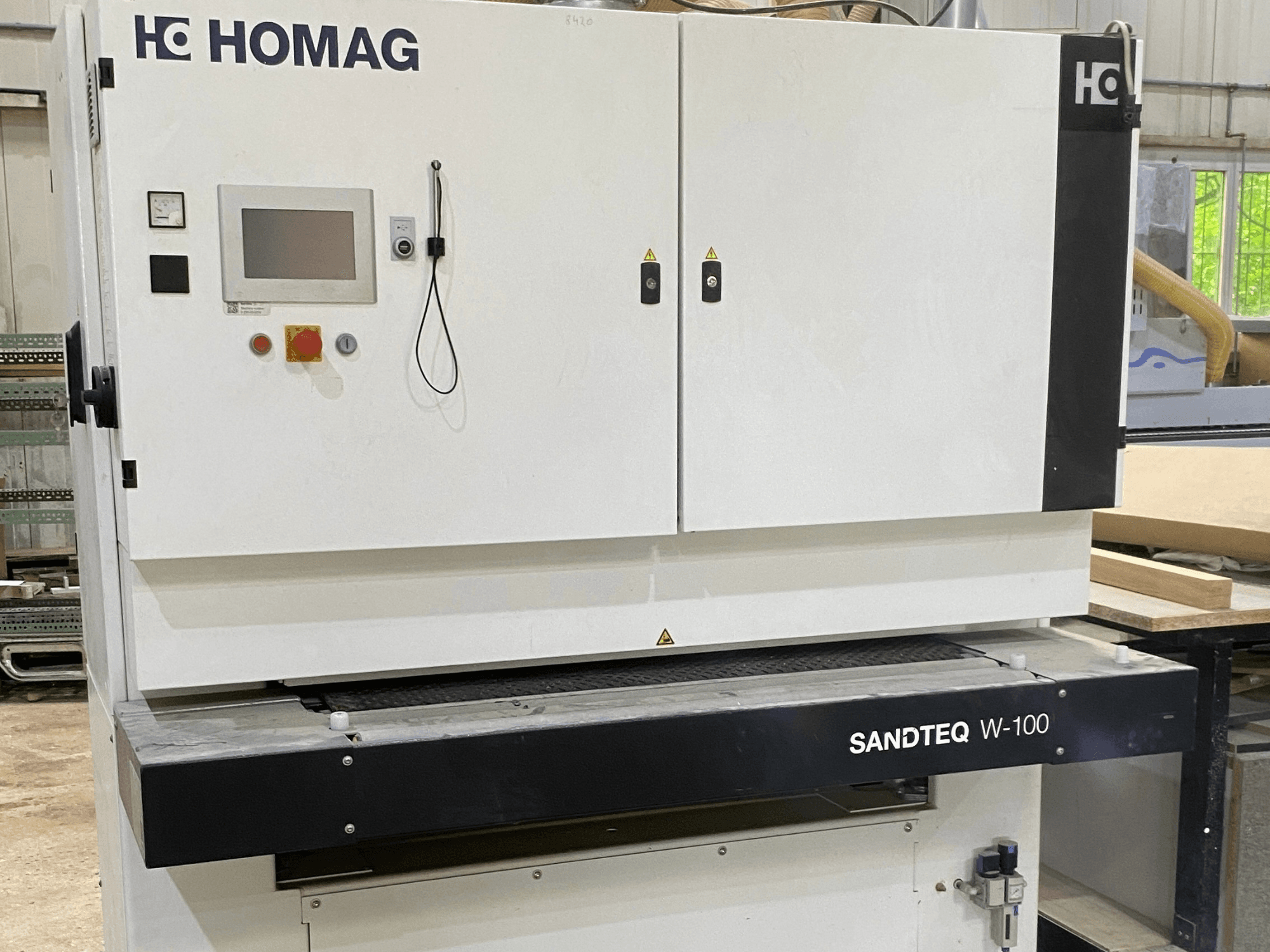 HOMAG SANDTEQ W-100 bandschuurmachine in een werkplaats, met daarop het bedieningspaneel, de stofafvoer en het schuurbandgedeelte. Vooraanzicht.